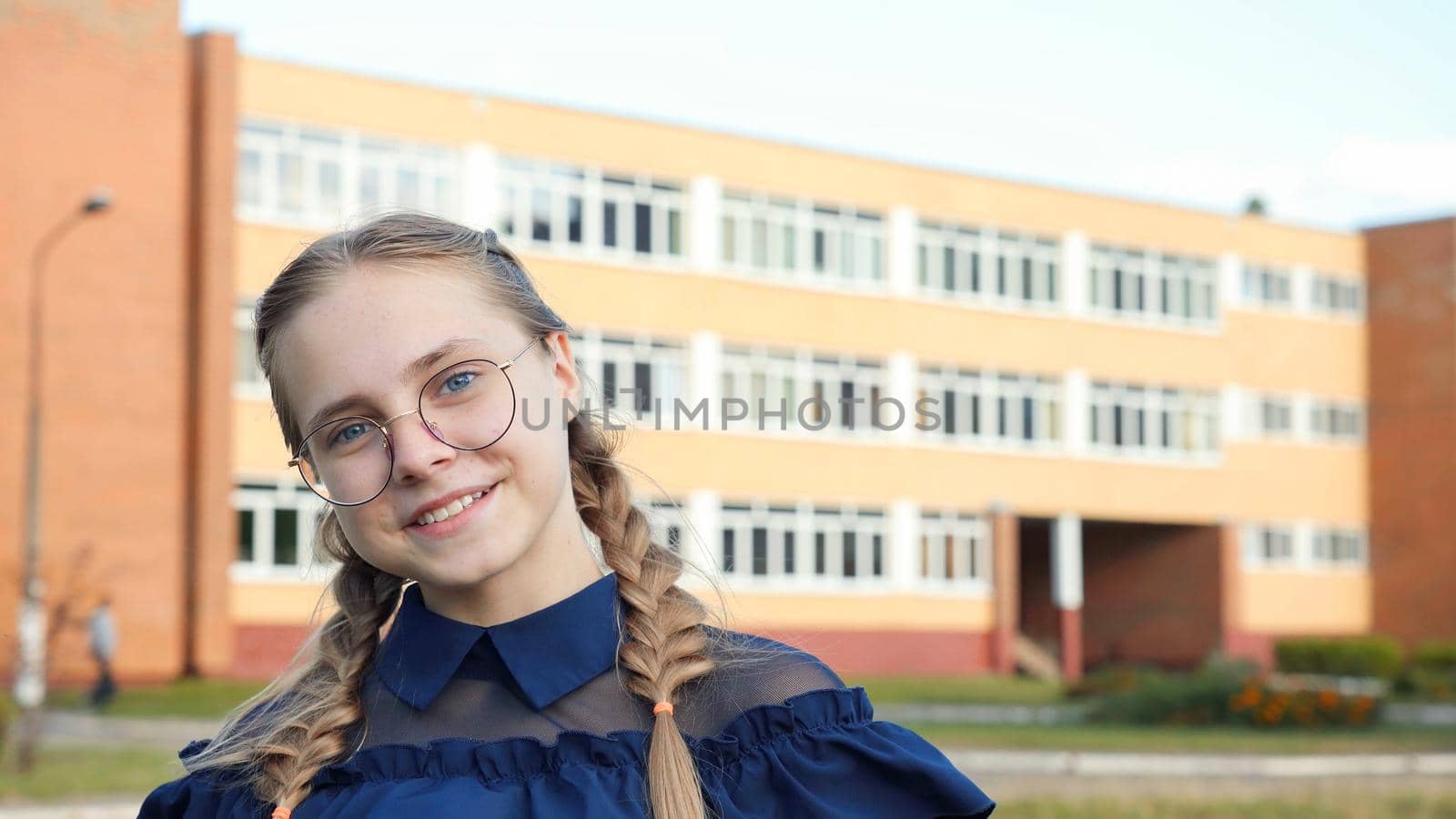 A teenage girl wearing glasses in front of a school