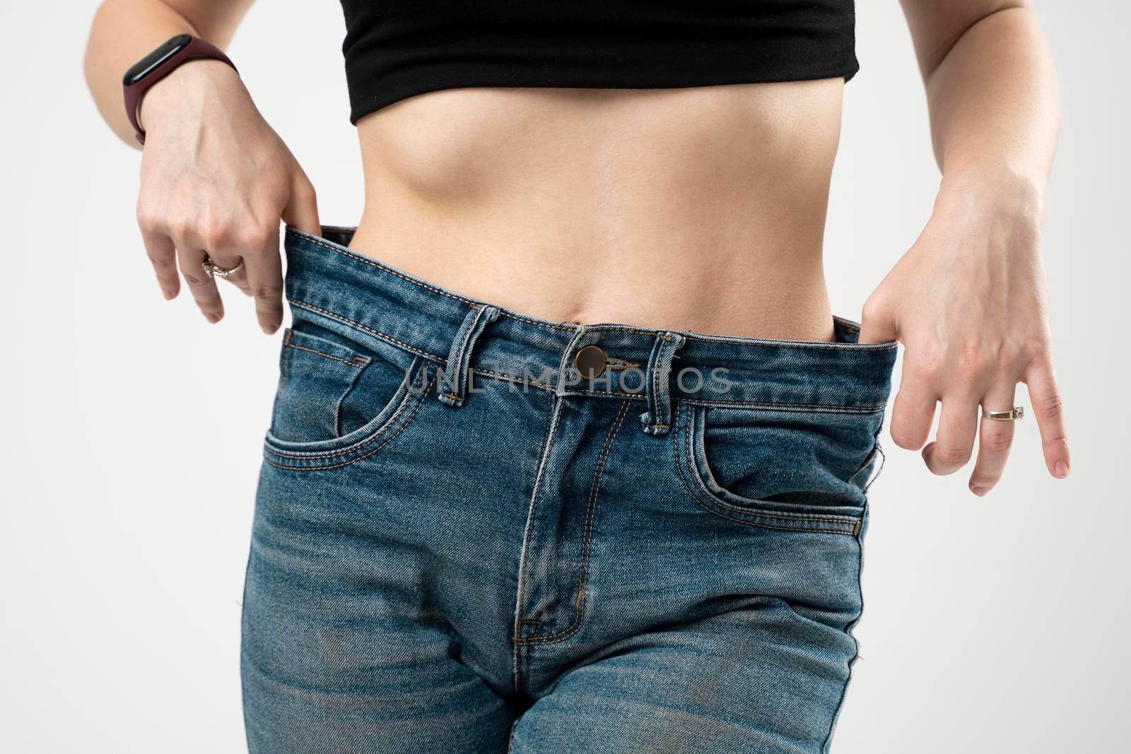Slim sporty woman in blue jeans showing a result of weight loss on white background. Diet concept and weight loss