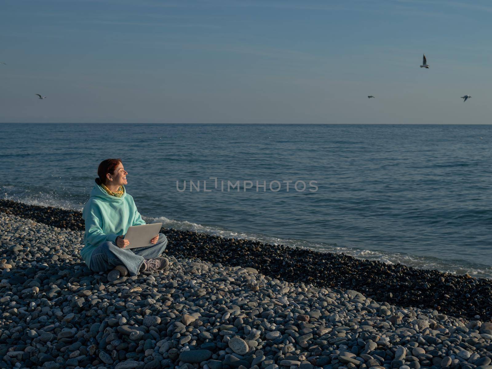 Happy caucasian woman working on a laptop while sitting on a pebble beach