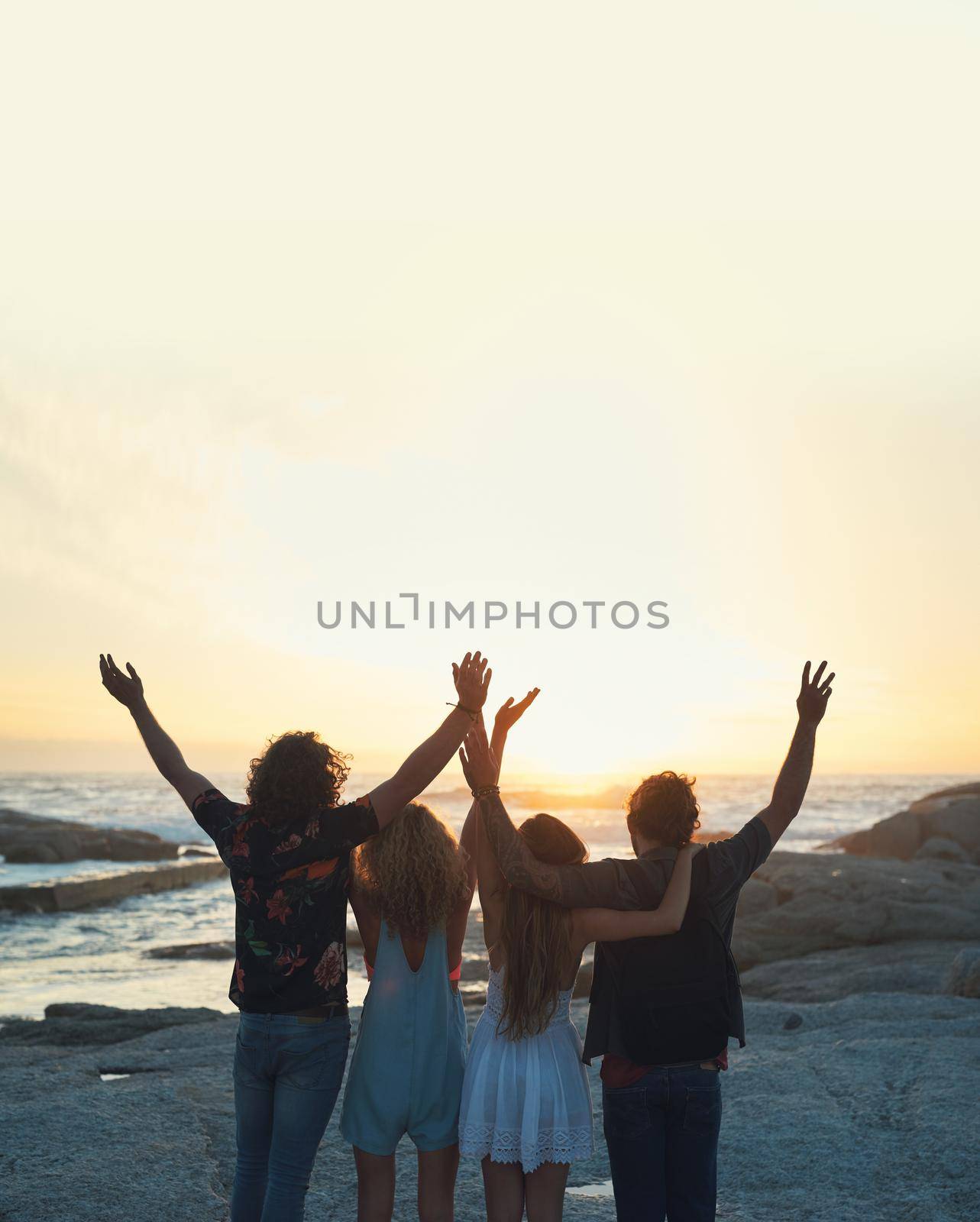 group of friends celebrating arms raised on beach looking at beautiful sunset enjoying summer vacation lifestyle.