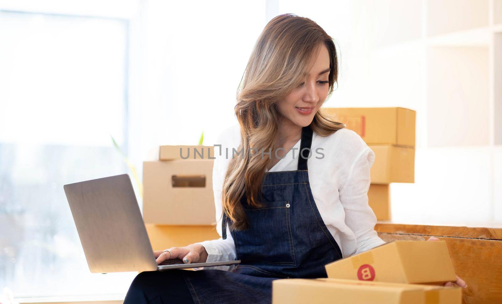 Portrait, entrepreneur, young Asian woman, freelance business, sme business, online shopping, working on laptop computer with parcel box on home office table, online business and delivery concept. by wichayada