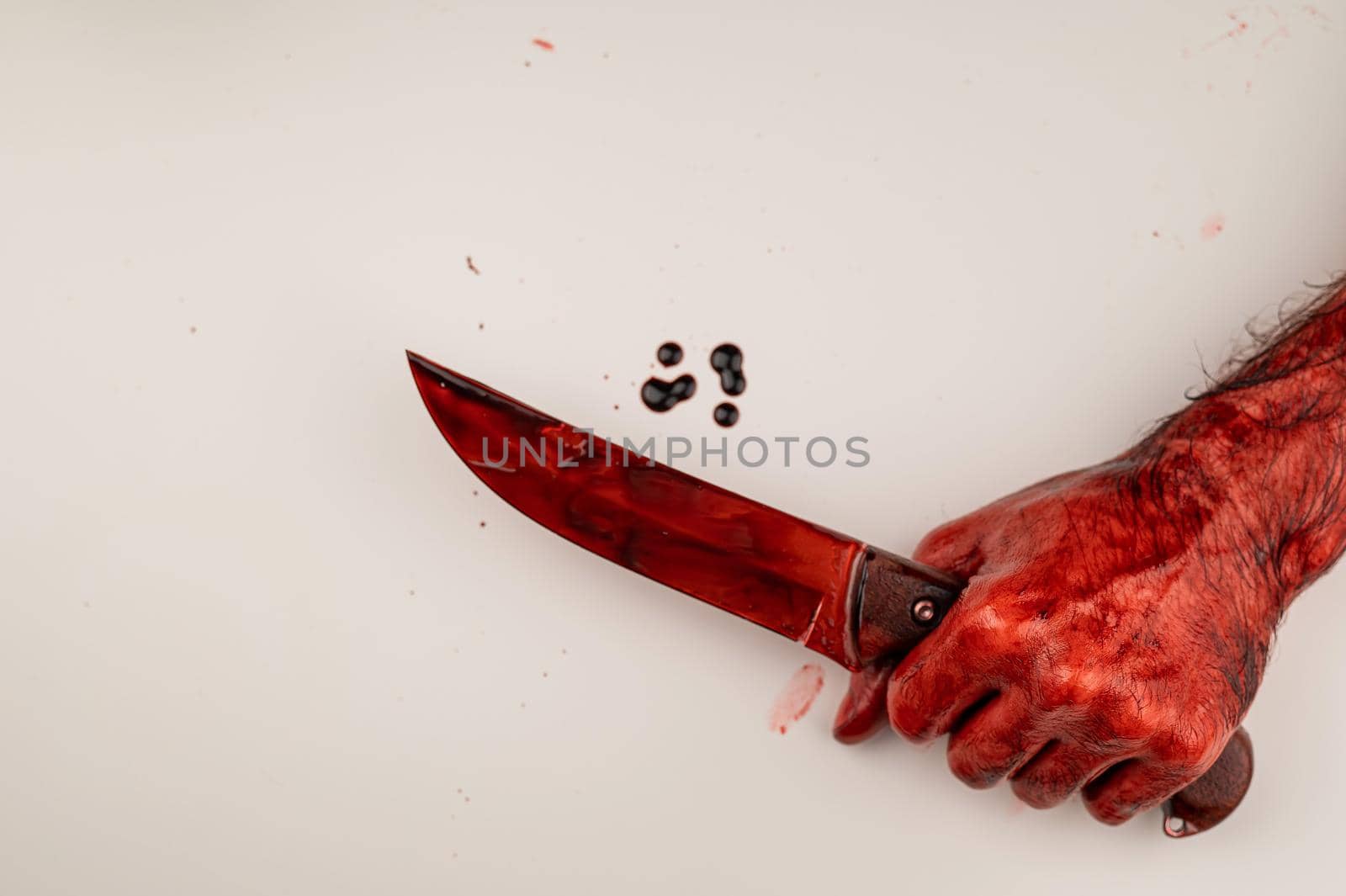 A man with bloody hands holds a knife on a white background