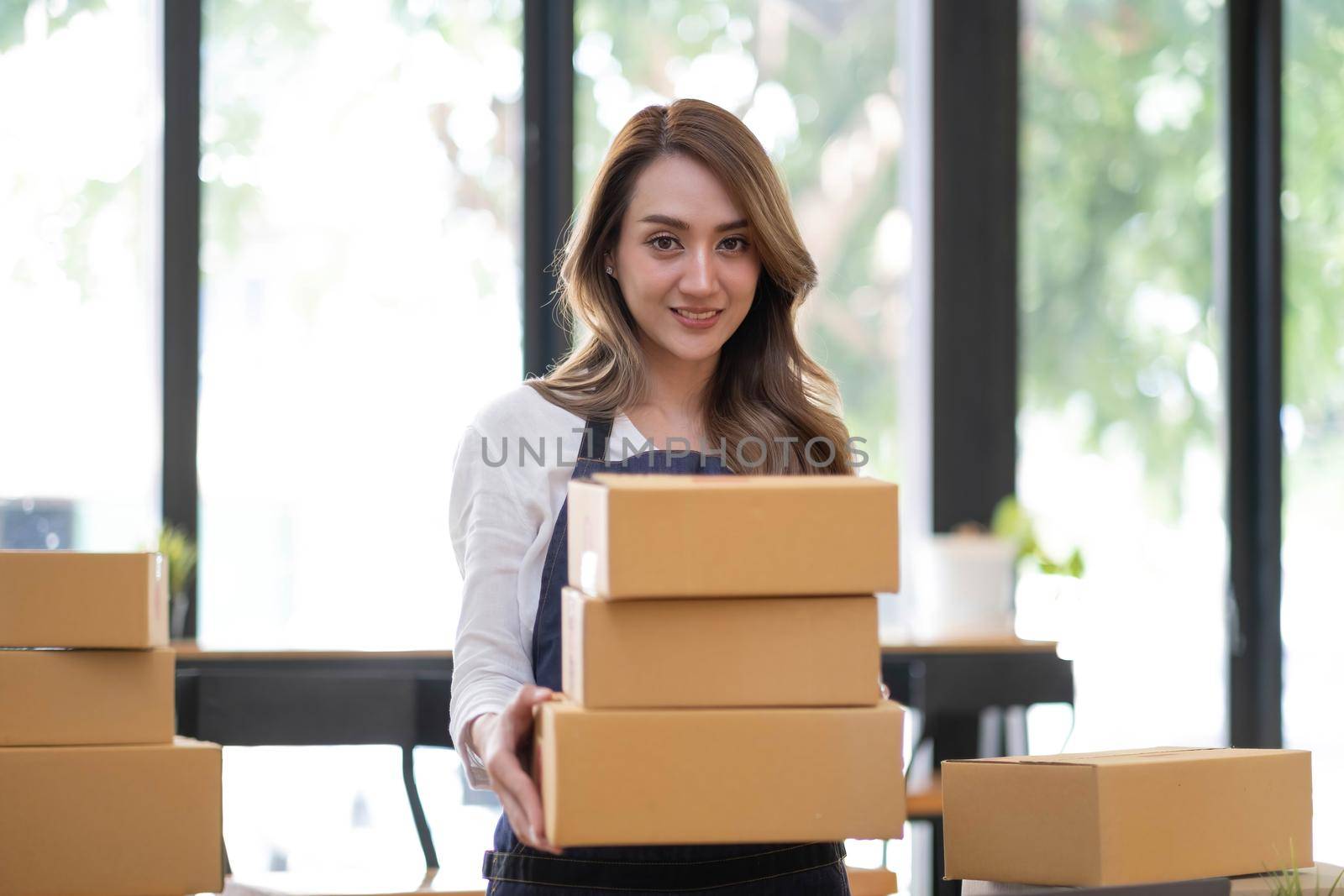 Portrait of Asian young woman SME working with a box at home the workplace.start-up small business owner, small business entrepreneur SME or freelance business online and delivery concept. by wichayada