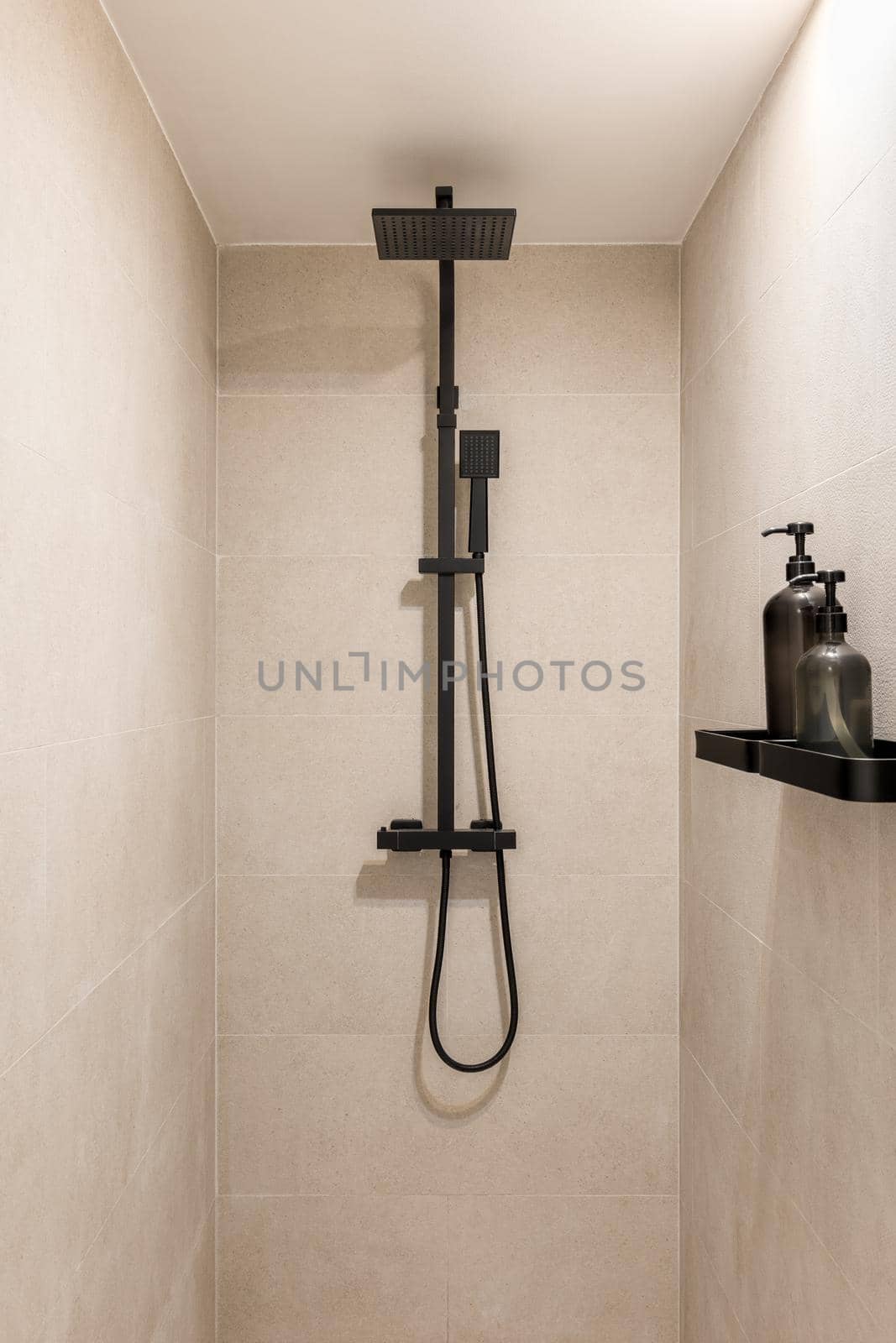 Black shower and ceramic tiled wall. Vertical view of modern minimalist interior of beige color.