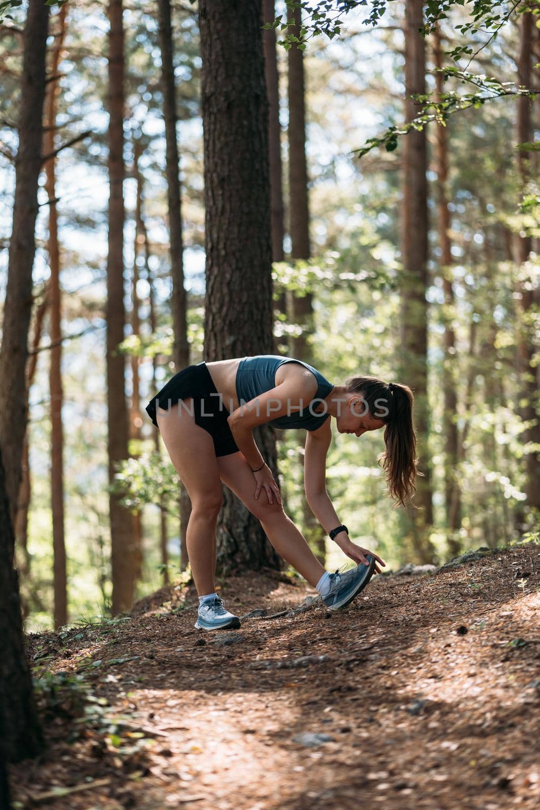 Young female runner stretching legs before running at morning forest trail. by apavlin