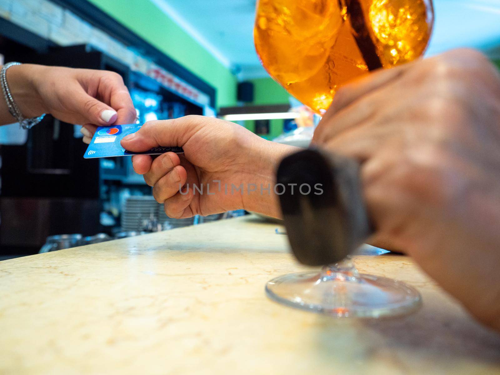 Customer paying for their order with a credit card in a cafe. Bartender holding a credit card reader machine and returning the debit card to female customer after payments.