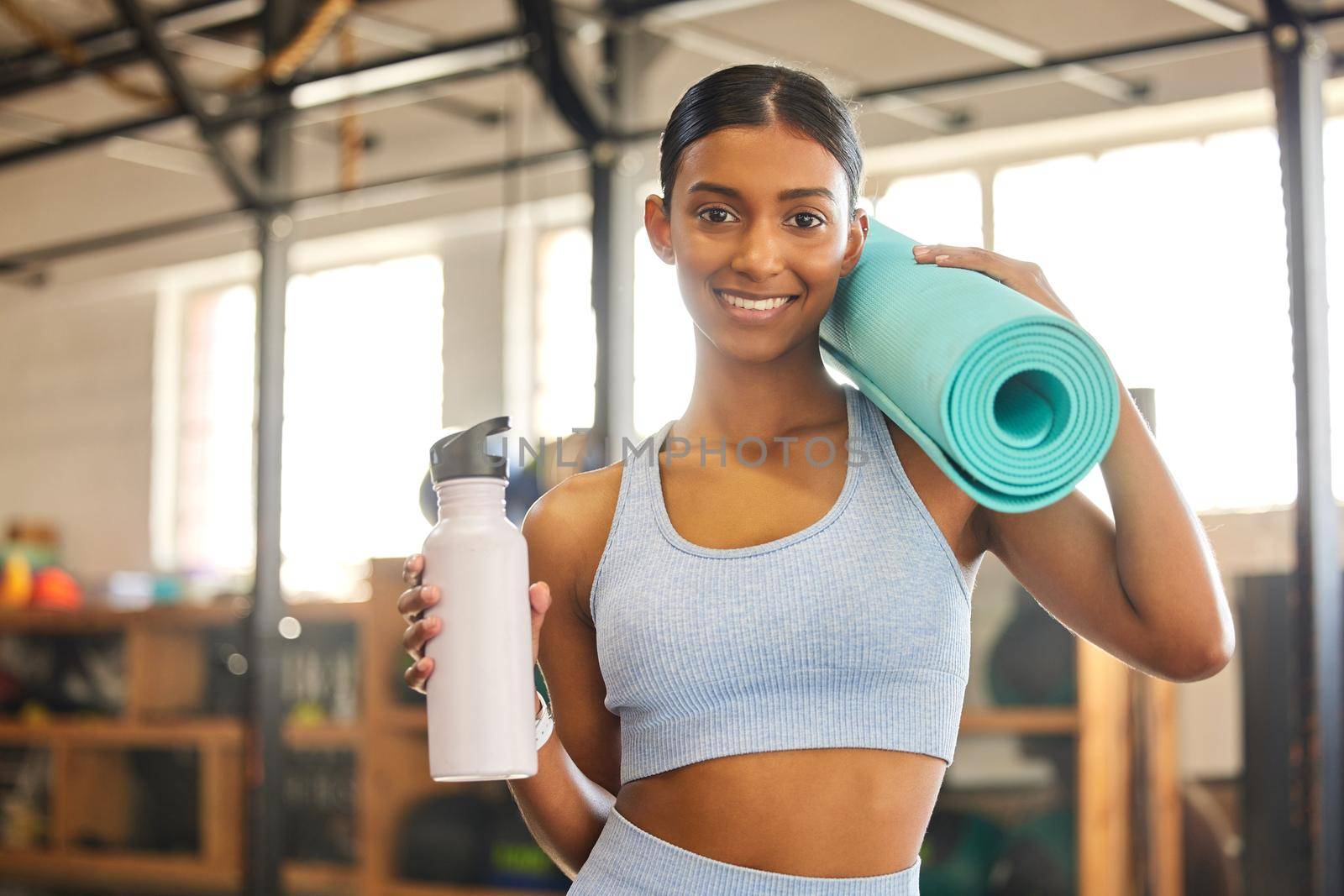 I reached my fitness goals and you can too. Portrait of a fit young woman holding an exercise mat and water bottle in a gym. by YuriArcurs