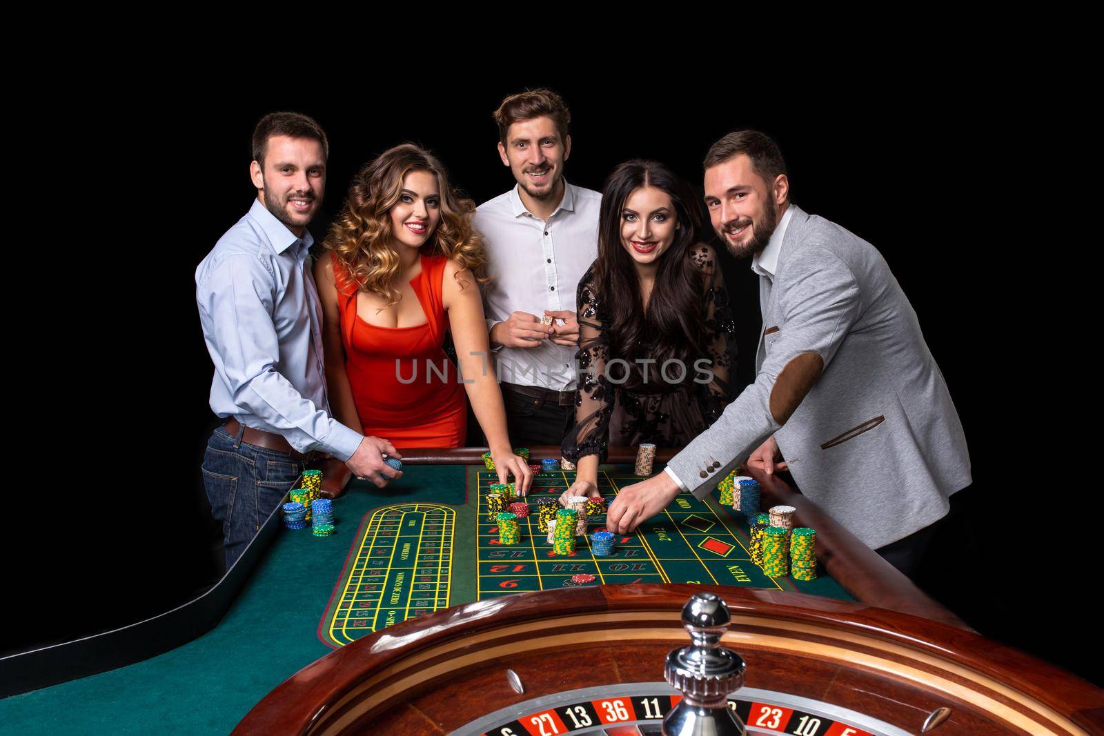 Group of young people behind roulette table in a casino. Black background