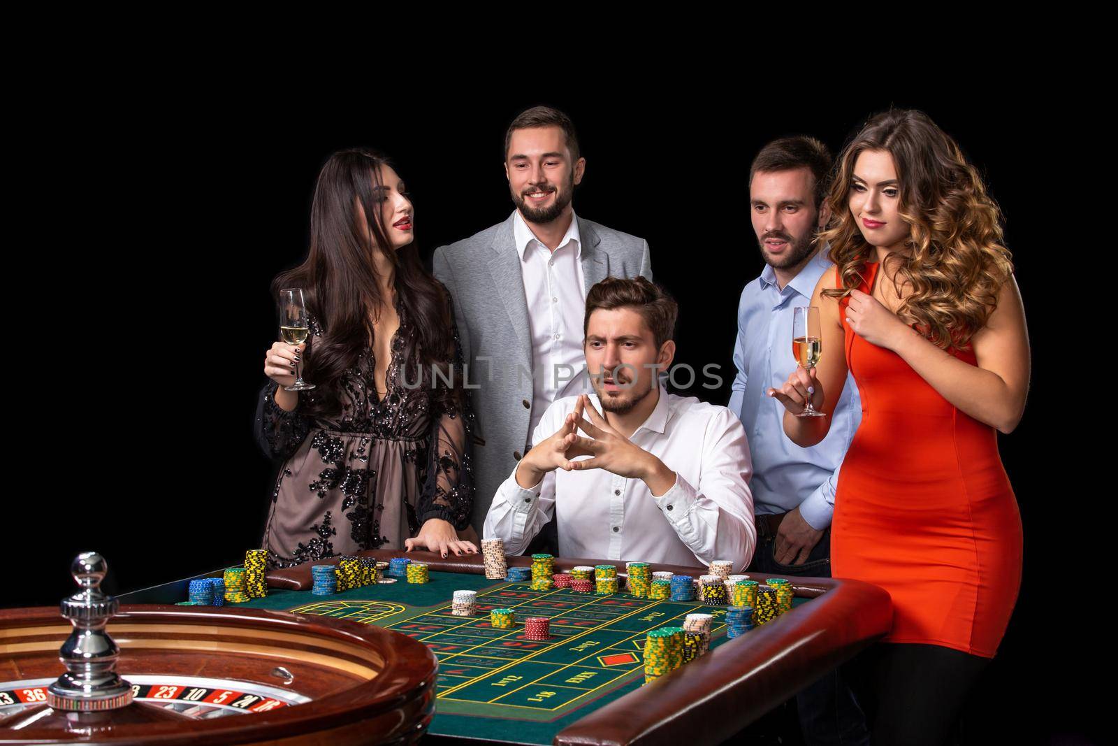 Group of young people looking excited at spinning roulette. Roulette table in a casino. Black background