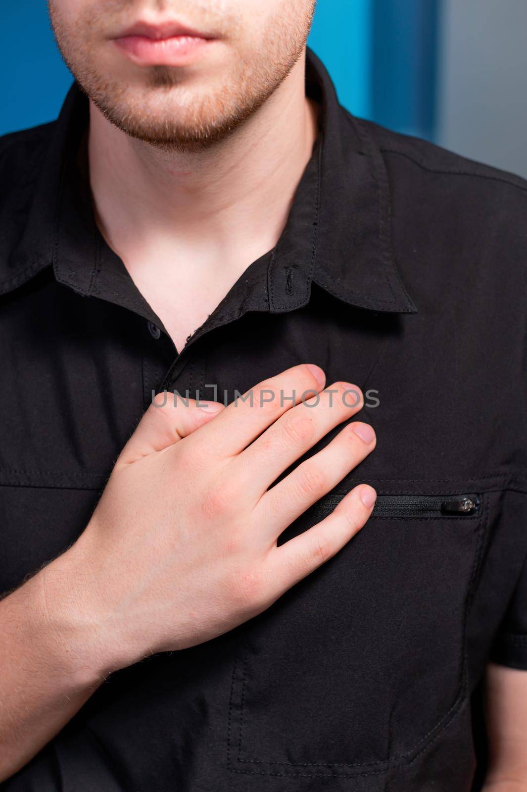 A young man stands and makes himself a lymphatic massage with his hand in the chest area, close-up.