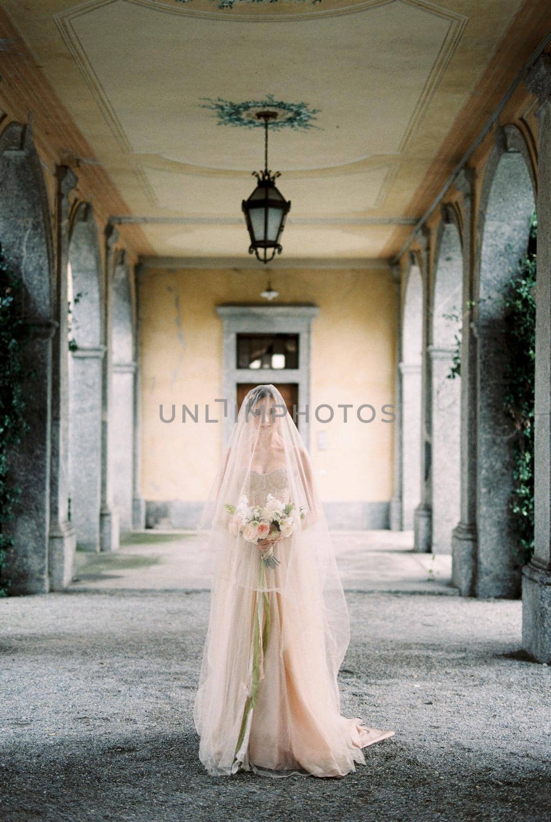 Bride in a dress with a veil stands with a bouquet on the terrace of an old villa. High quality photo
