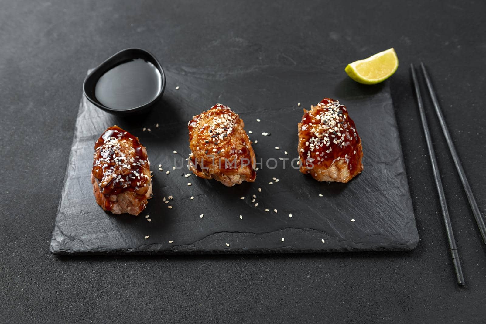 Asian appetizer. Chinese cuisine chicken in sweet and sour sauce on a black background. Chicken with teriyaki sauce and sesame seeds. Next to it are chopsticks and soy sauce.