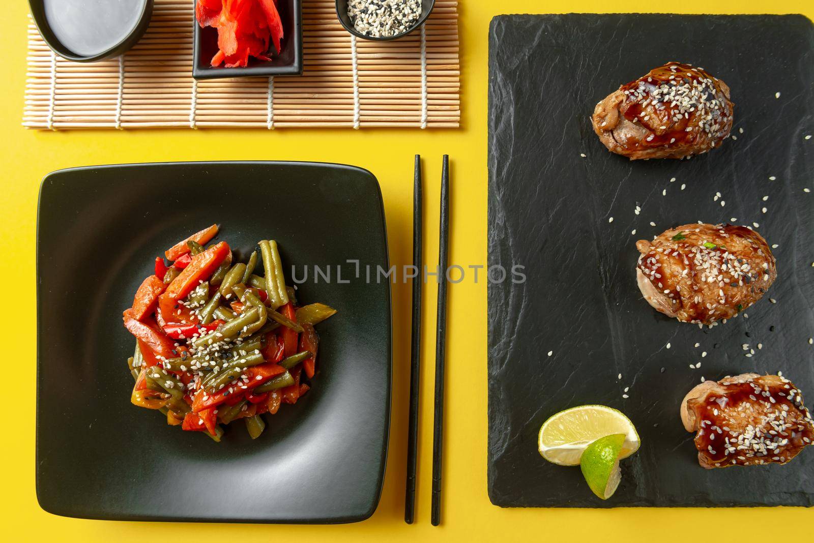 A variety of Asian food on a bright yellow background. Chinese fried vegetables with other Asian food on a yellow background. Teriyaki chicken and roasted Korean vegetables. Asian food mix.
