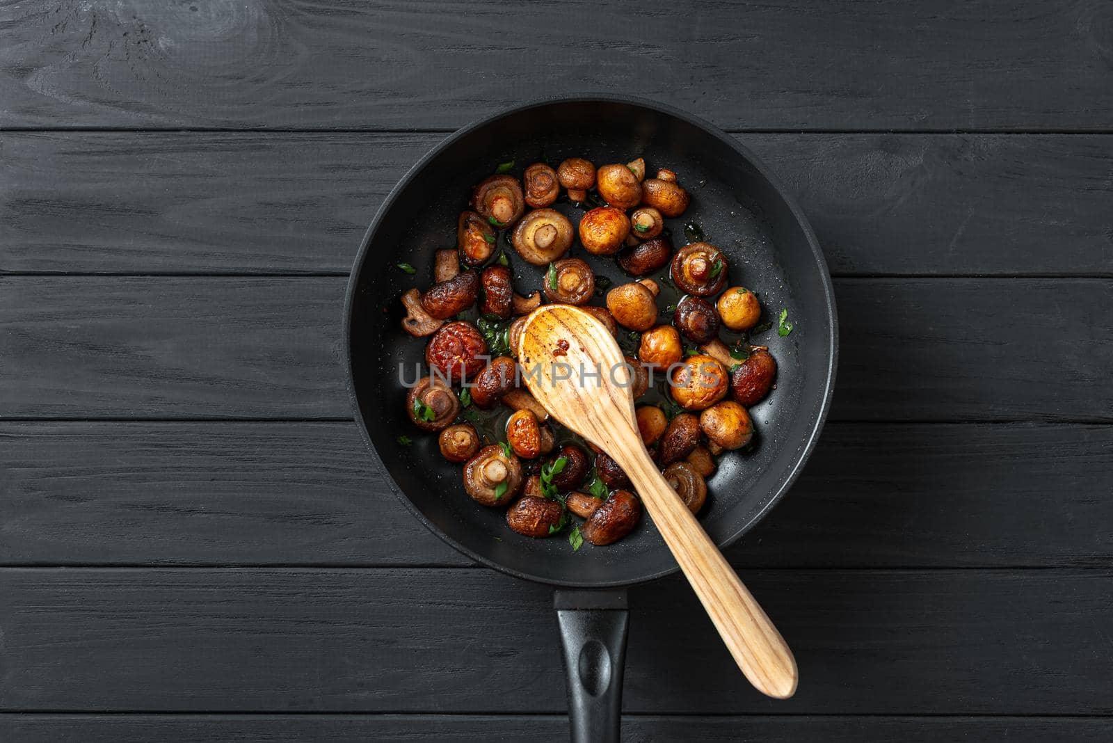 Pan of fried mushrooms champignons on a dark wooden background. Top view. Place for text and copy space