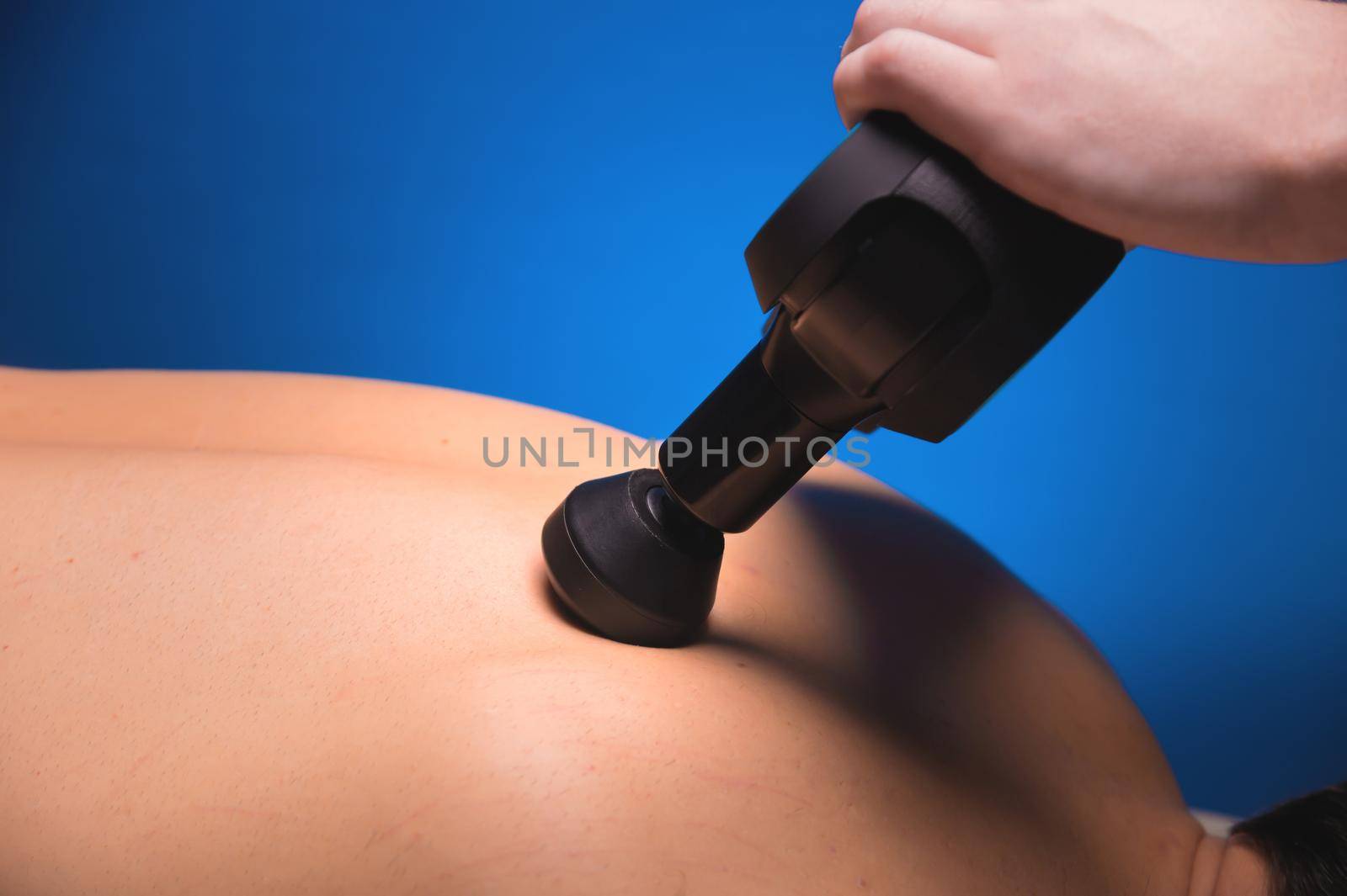 Physiotherapist treats the spine and back of a man with a massage percussion device. Physiotherapy, close-up, massage therapist by yanik88