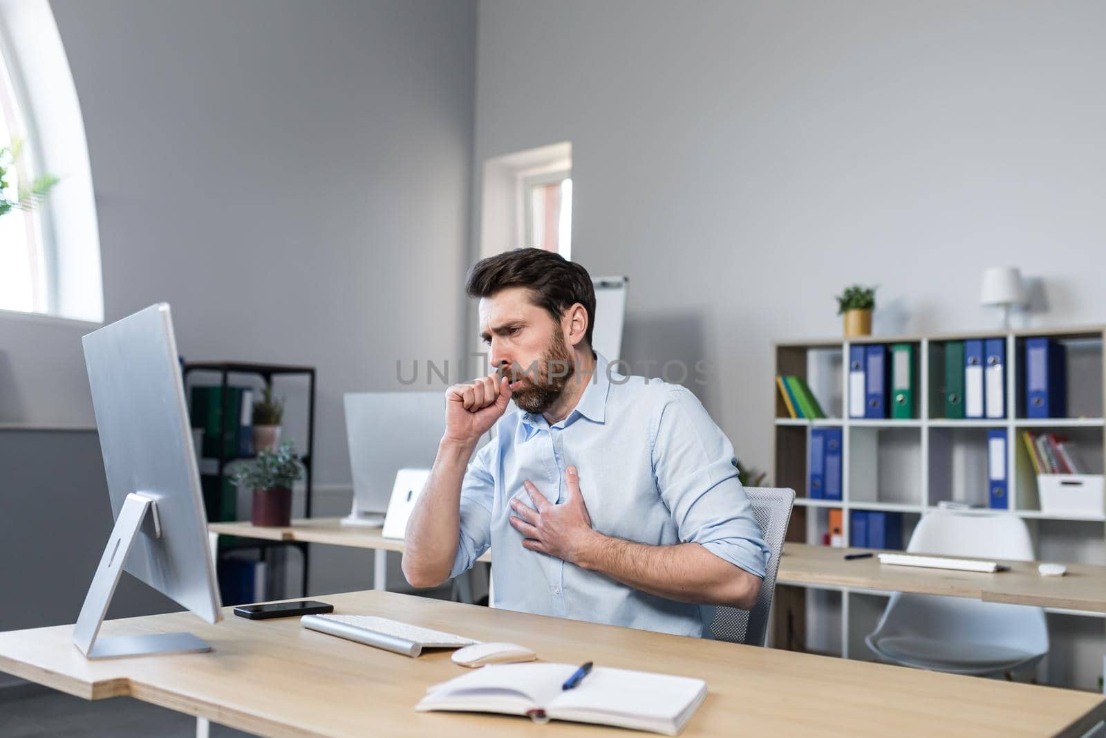 Sick man working in the office, has a bad cough, coughing businessman at the computer by voronaman