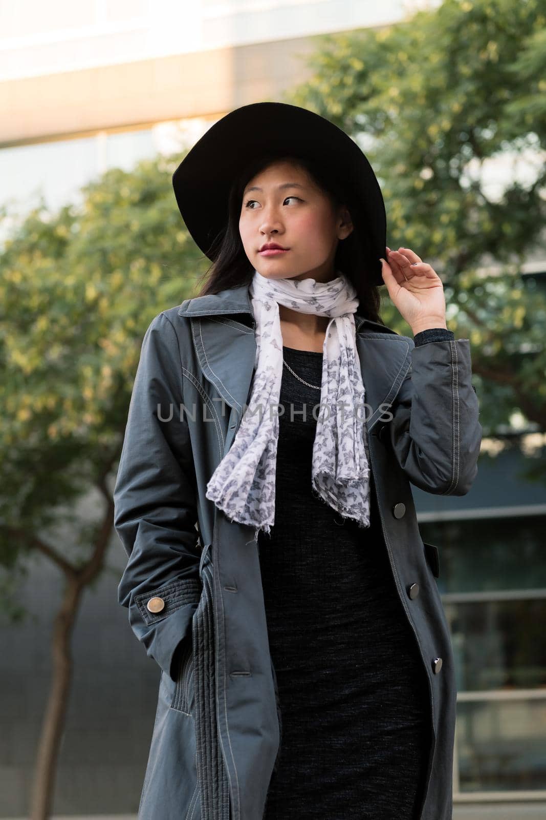 vertical portrait of a classy asian woman with hat and trench coat in the city, concept of elegance and urban lifestyle