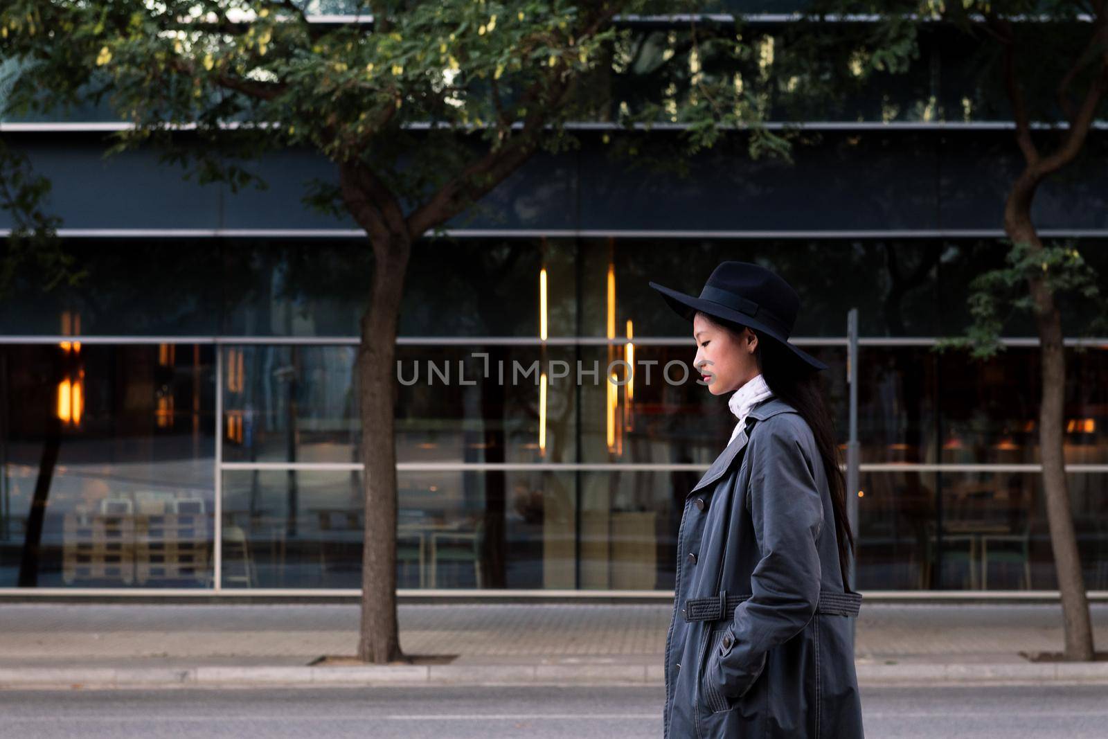elegant asian woman in hat and trench coat walking in the city, urban lifestyle concept, copy space for text