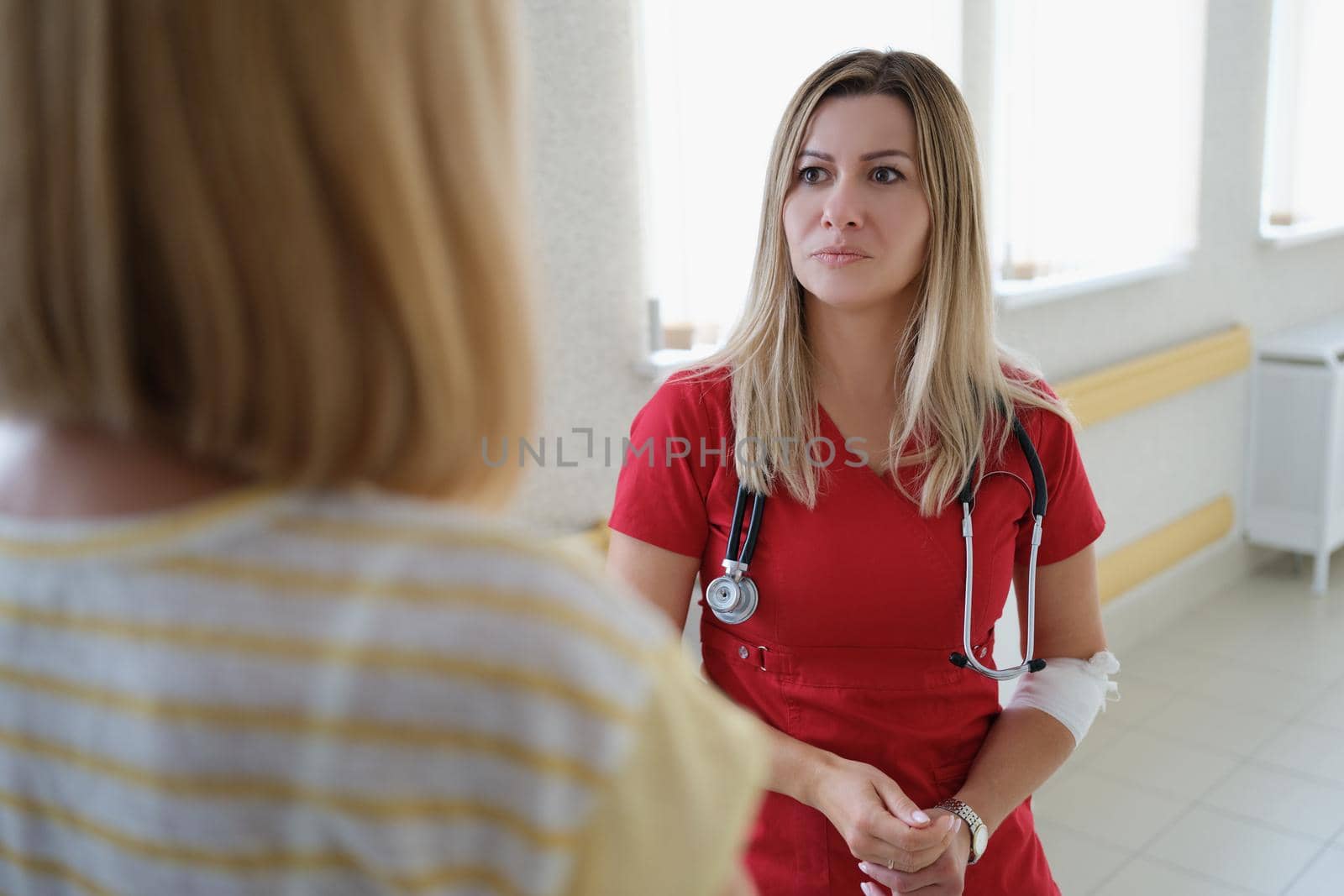 Female therapist doctor in red uniform consults and listens to patient in clinic. Doctor makes recommendations and explains results of medical examination at meeting concept