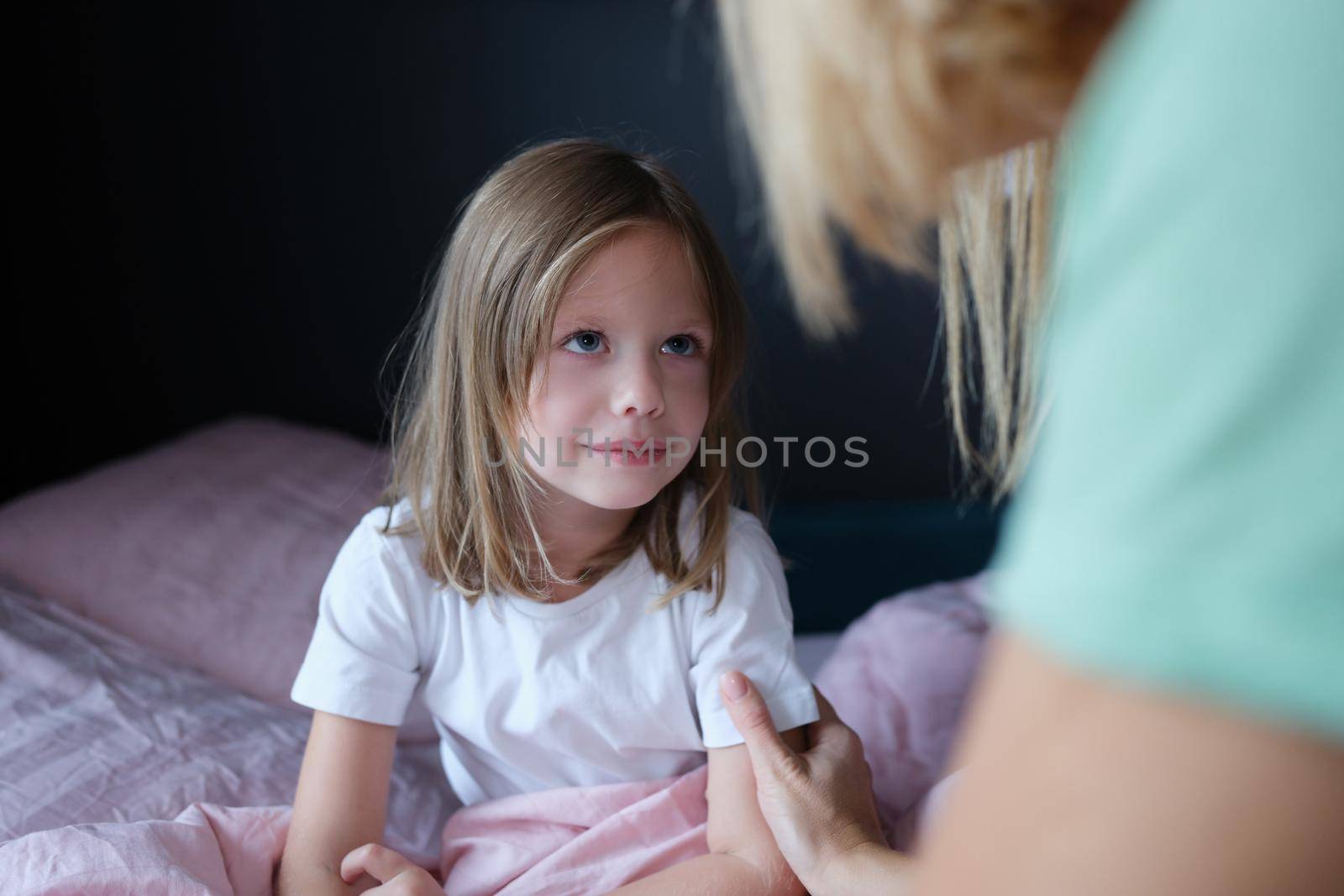 Mother holds the hand of a cute girl daughter and talking sitting at home in bed. Caring older sister mother or nanny is having friendly confidential conversation with little daughter of preschool age