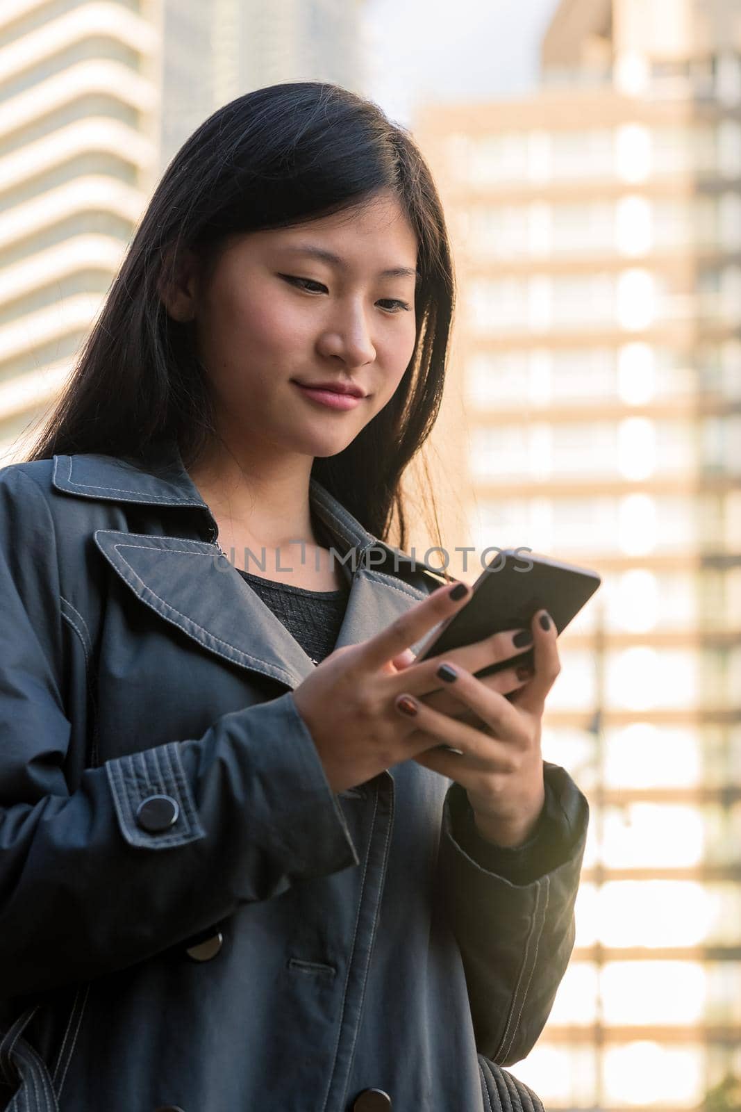 vertical photo of an elegant young asian woman consulting her mobile phone in the city, technology and urban lifestyle concept