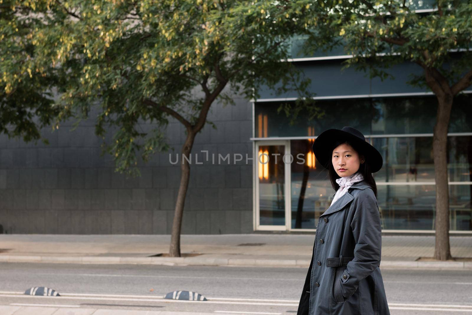 elegant asian woman in hat and trench coat walking in the city, urban lifestyle concept, copy space for text