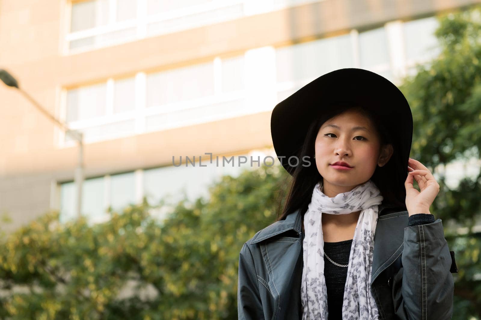 portrait of a classy asian woman with hat and trench coat in the city, concept of elegance and urban lifestyle, copyspace for text