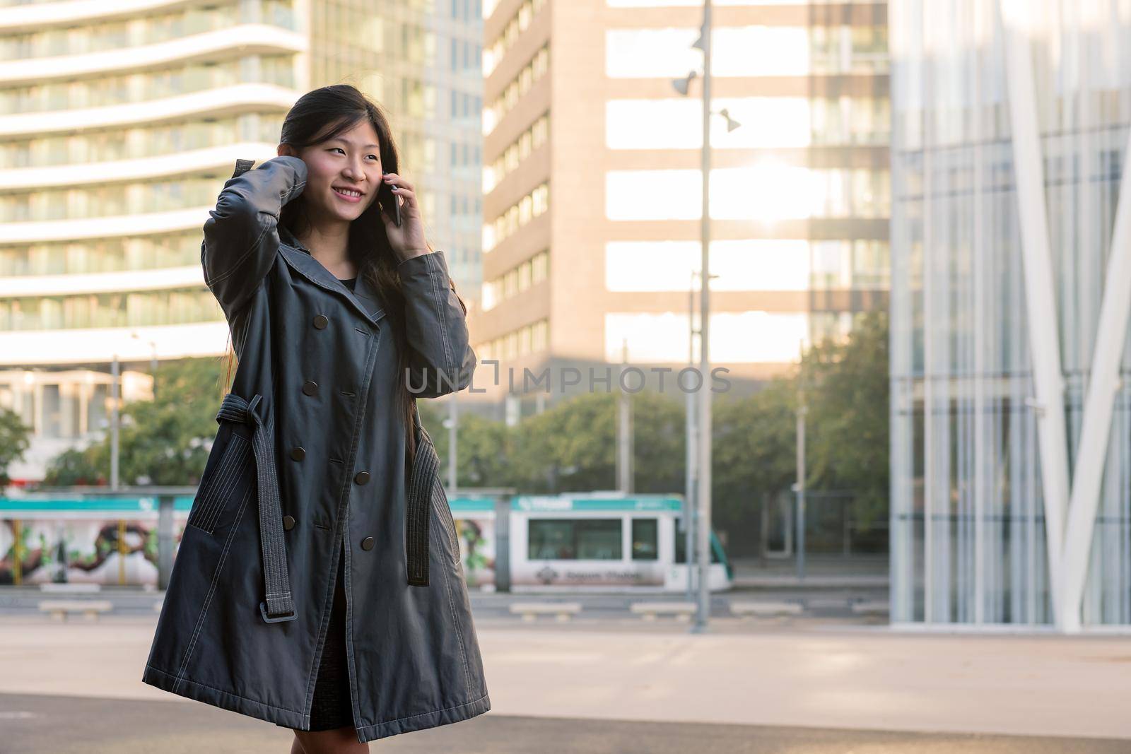 smiling young asian woman talking by mobile phone while walking in the city, technology and urban lifestyle concept, copy space for text