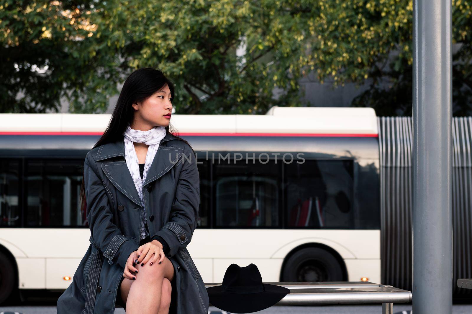 asian woman sitting and waiting for the bus al the bus stop, concept of public transportation and urban lifestyle
