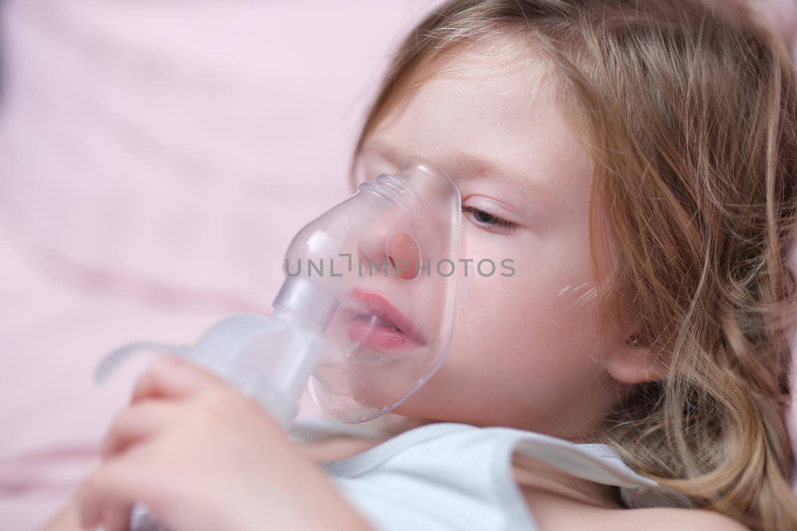 Little baby girl with oxygen mask lying on hospital bed or at home. Upset sad sick child breathing oxygen mask concept