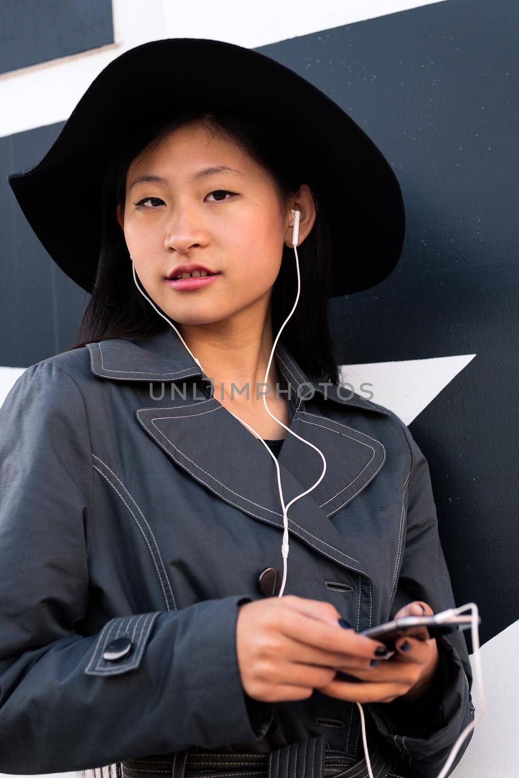 vertical portrait of a beautiful classy chinese girl with earphones listening music from her phone, concept of technology and modern lifestyle