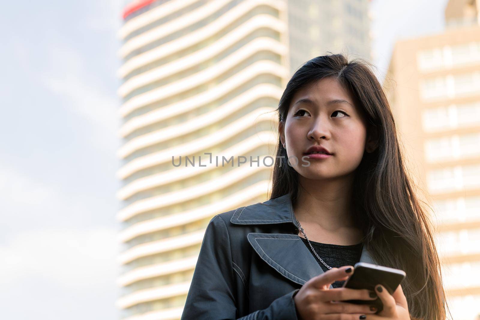 young asian woman consulting her cell phone in the downtown, technology and urban lifestyle concept, copy space for text