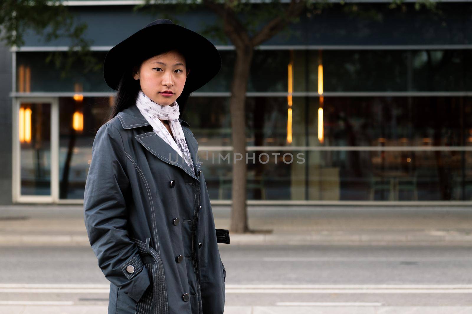 portrait of a beautiful asian woman in hat and trench coat in the city, concept of elegance and urban lifestyle, copy space for text