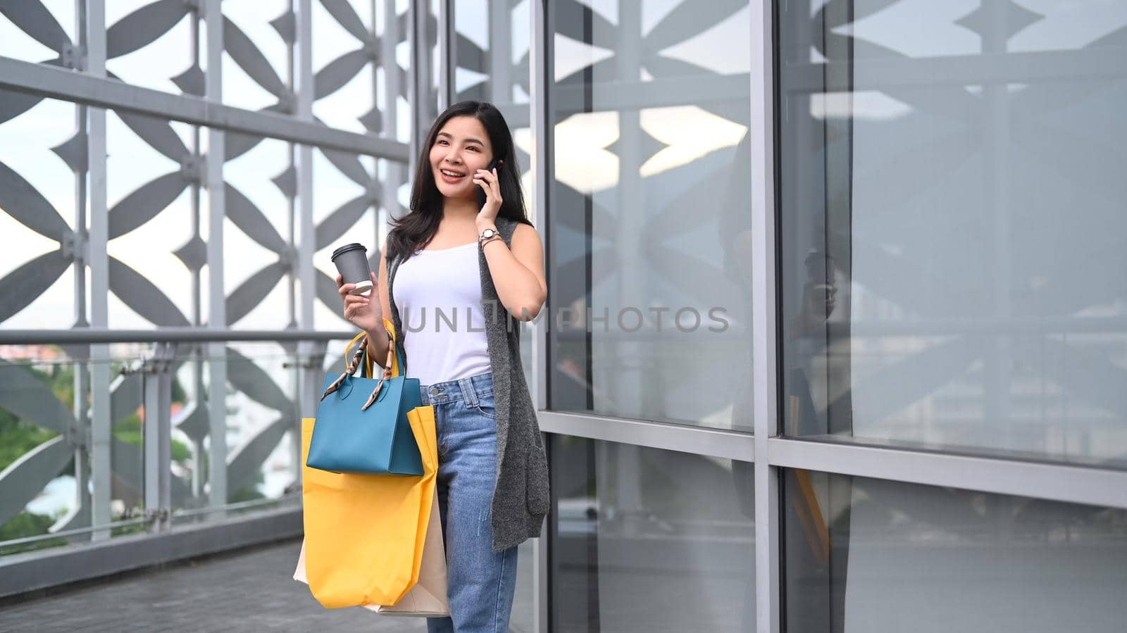 Stylish young woman with shopping bags and talking on mobile phone, walking outside shopping mall.
