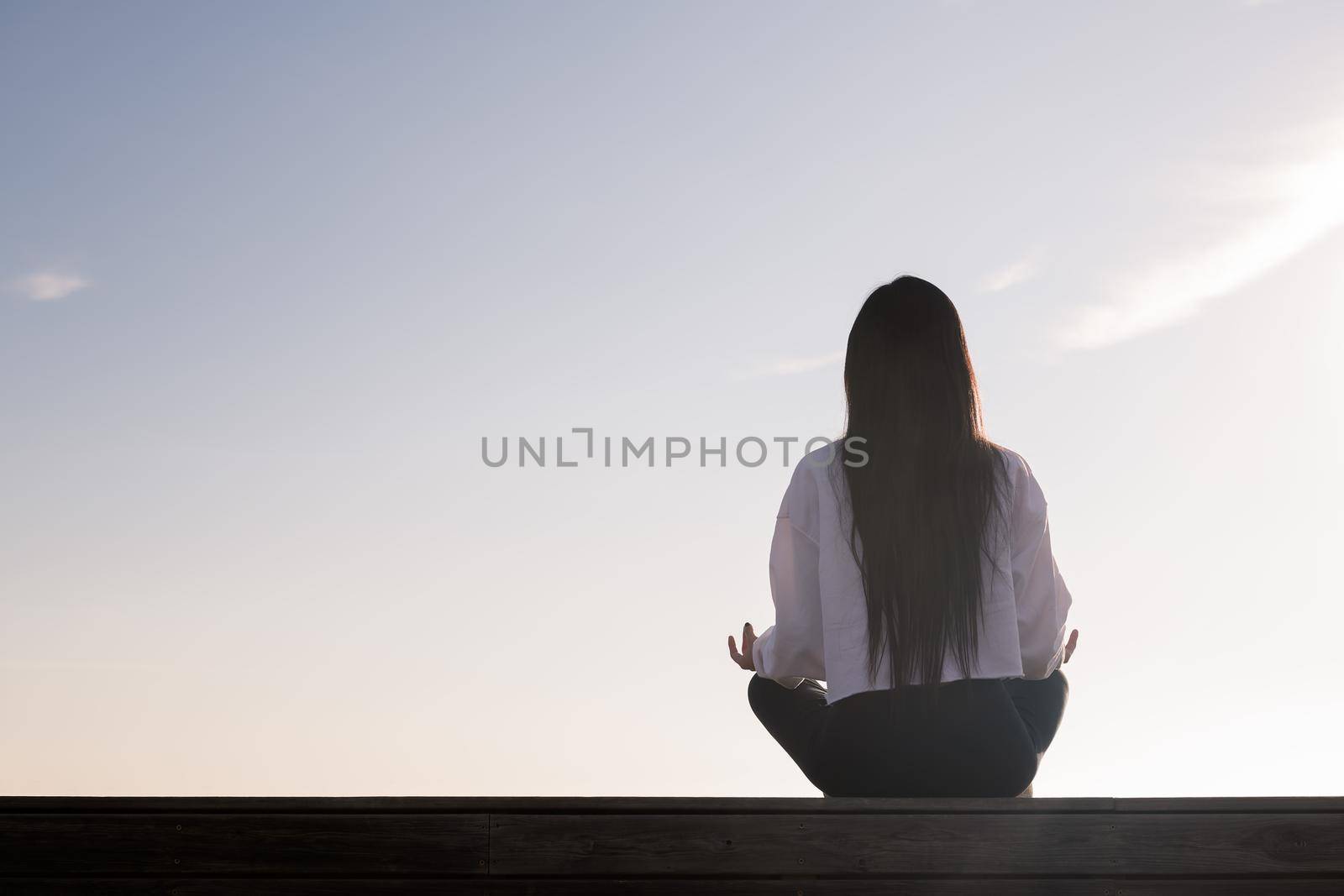 rear view of a young woman with long hair meditating at sunrise, concept of relaxation and mental health, copy space for text