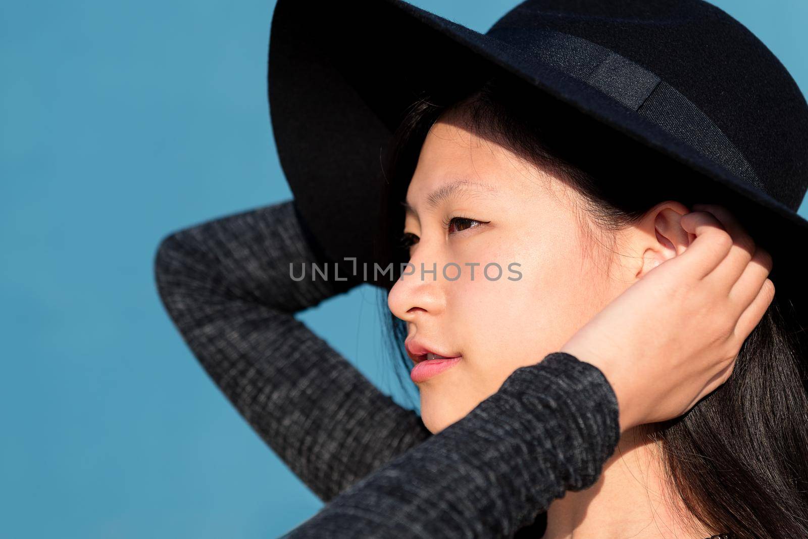 profile portrait of an elegant and beautiful asian woman in a hat on blue background, concept of fashion and lifestyle, copyspace for text