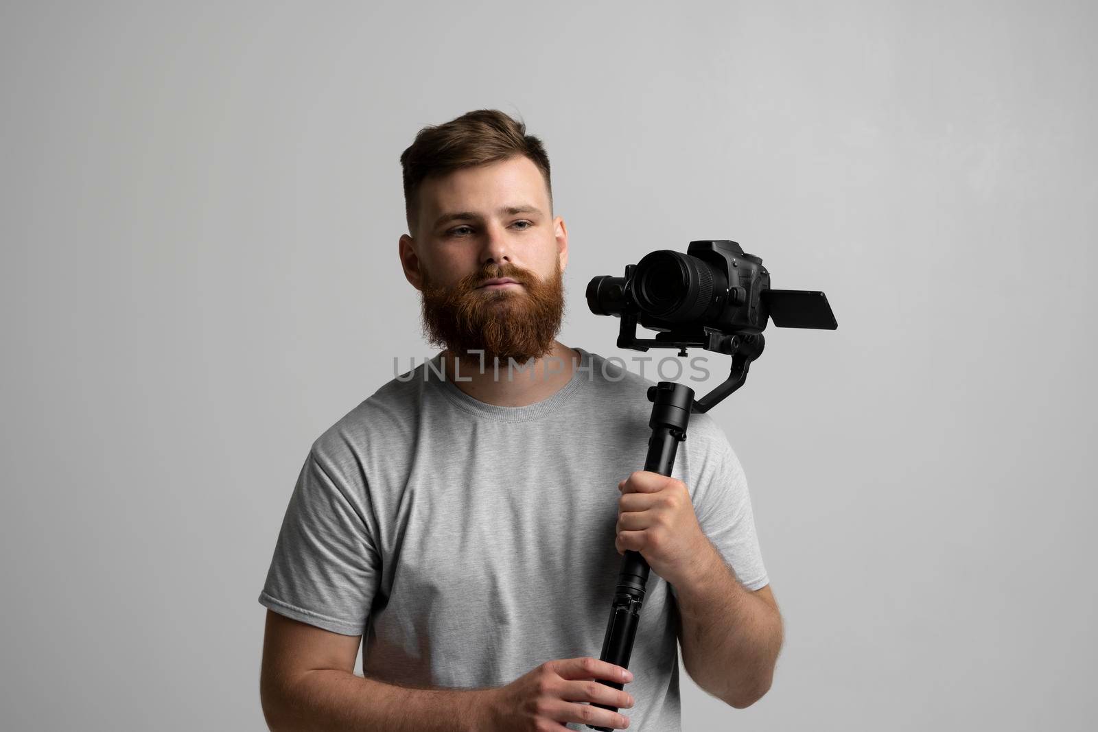 Handsome bearded videographer making a good footage using steadicam. Cameraman creator with a stabilizer in his hands takes a video on the slr video camera on white background