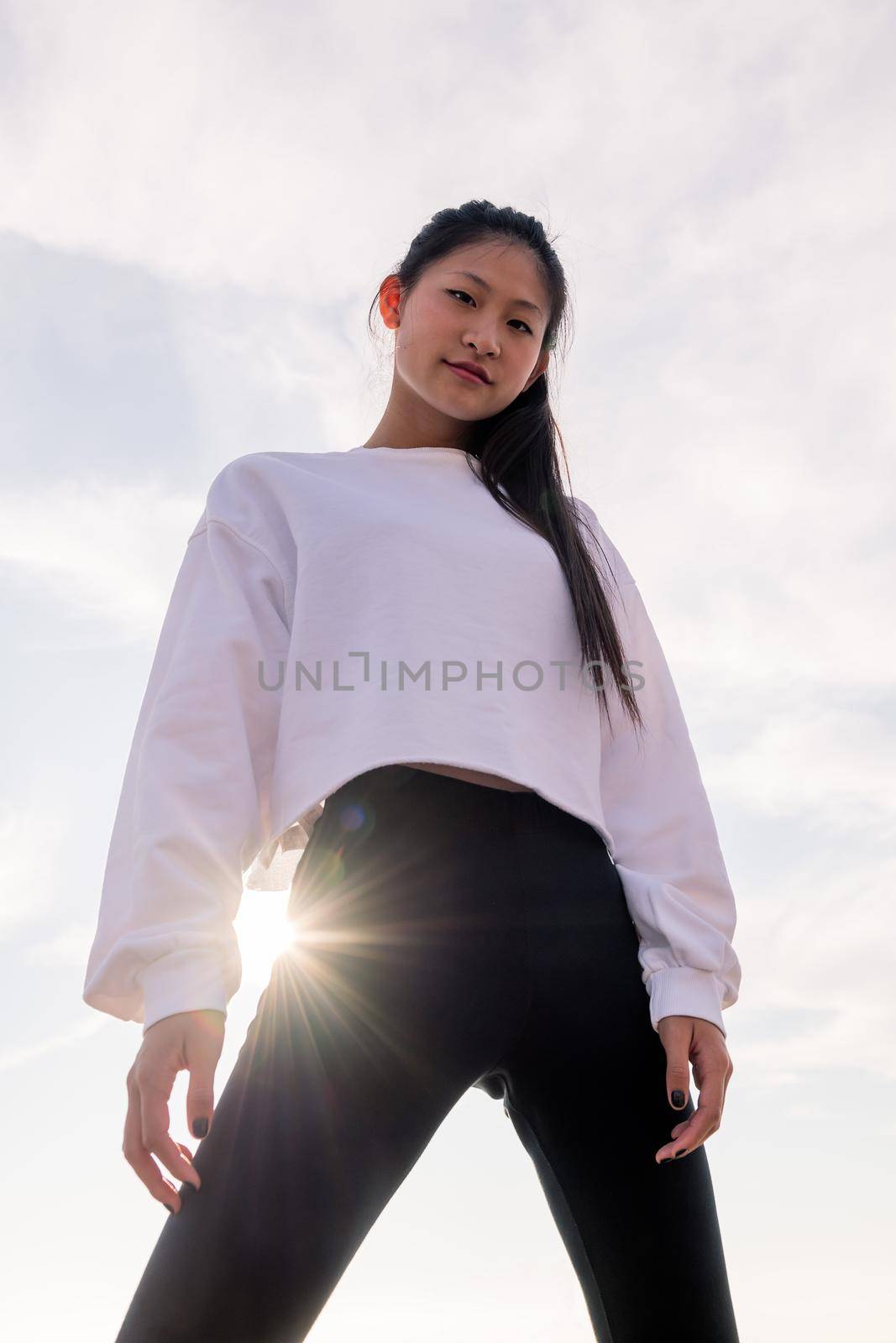 vertical photo of a powerful asian sportswoman posing confident smiling defiant at camera, concept of sport and healthy lifestyle, copyspace for text