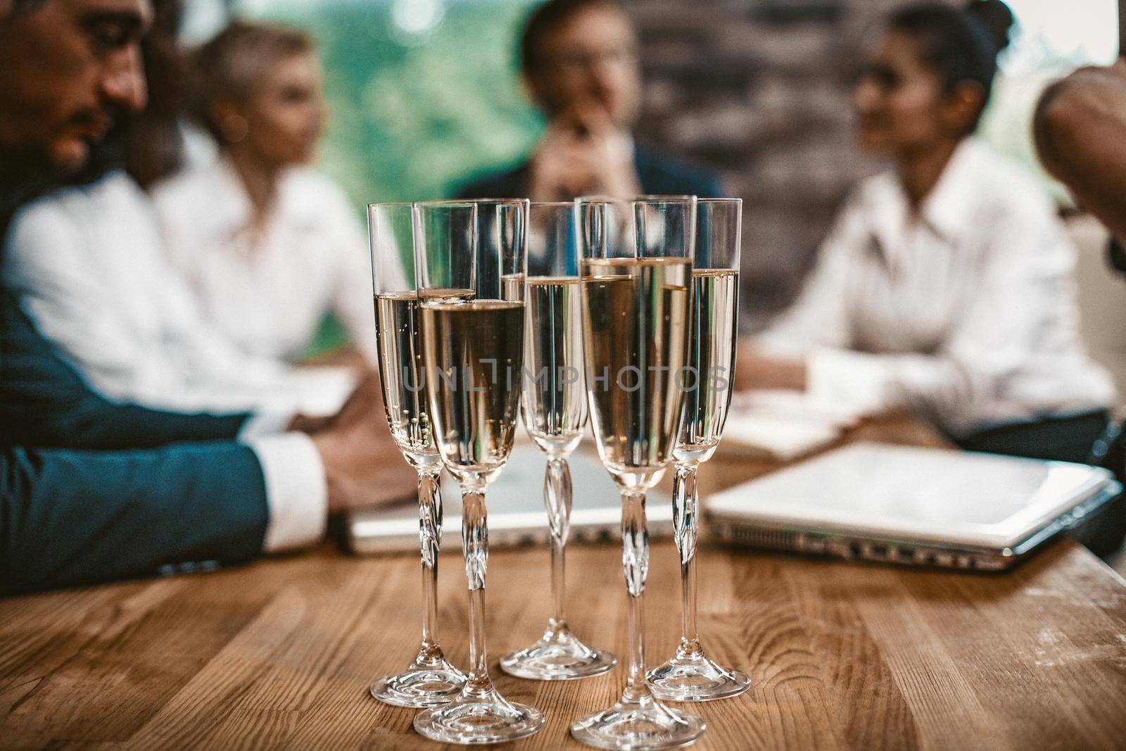 Glasses With Champagne Are On Wooden Table, Selective Focus On Five Glasses With Alcohol In The Foreground, Business Partners Communicate On A Blurred Background, Business Event Concept, Toned Image