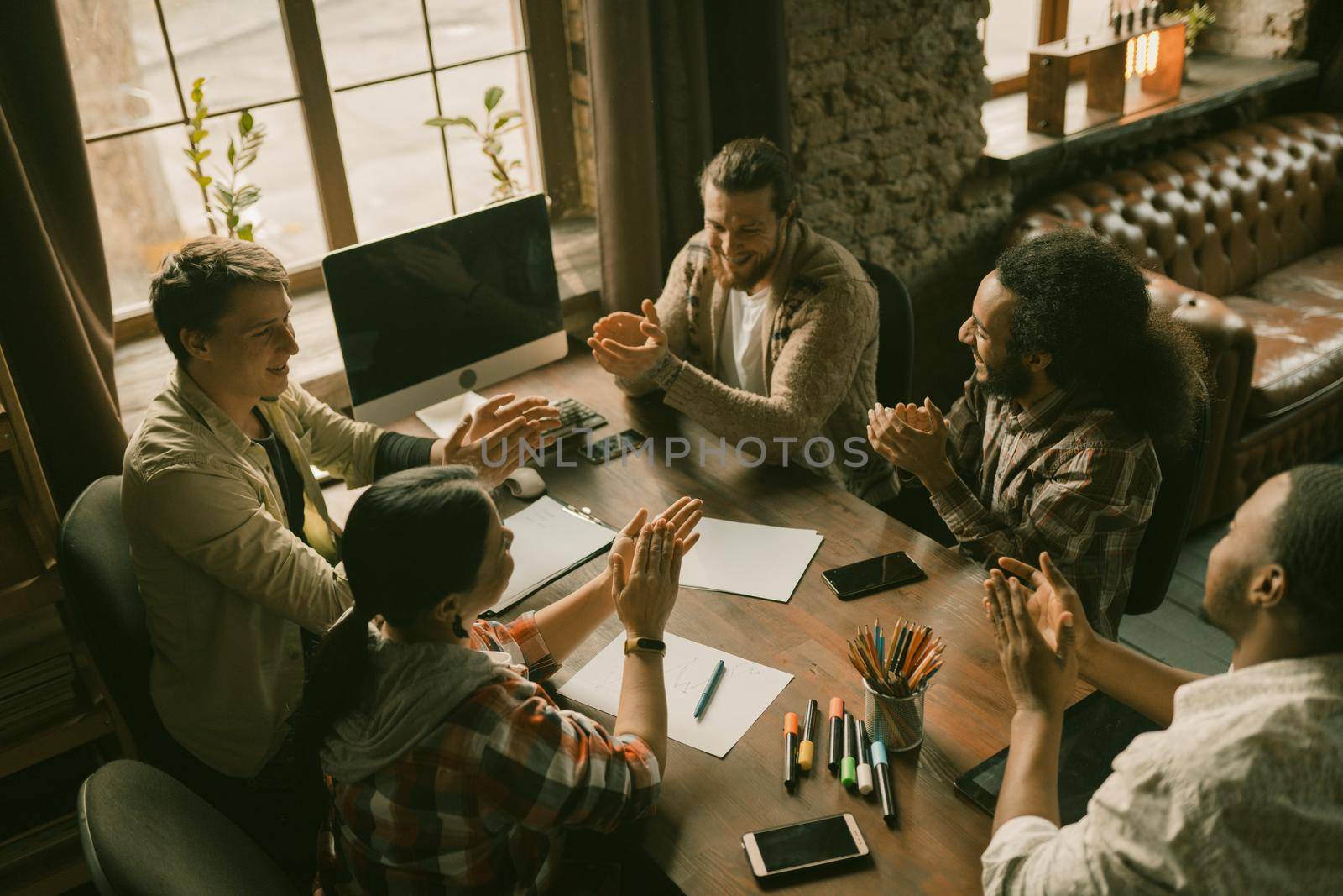 Cheerful Colleagues Claping Their Hands Together, Multi-Ethnic Group Of Coworkers Have Fun Applauding Each Other Sitting At Wooden Table Near Window In Coworking Space, High Angle