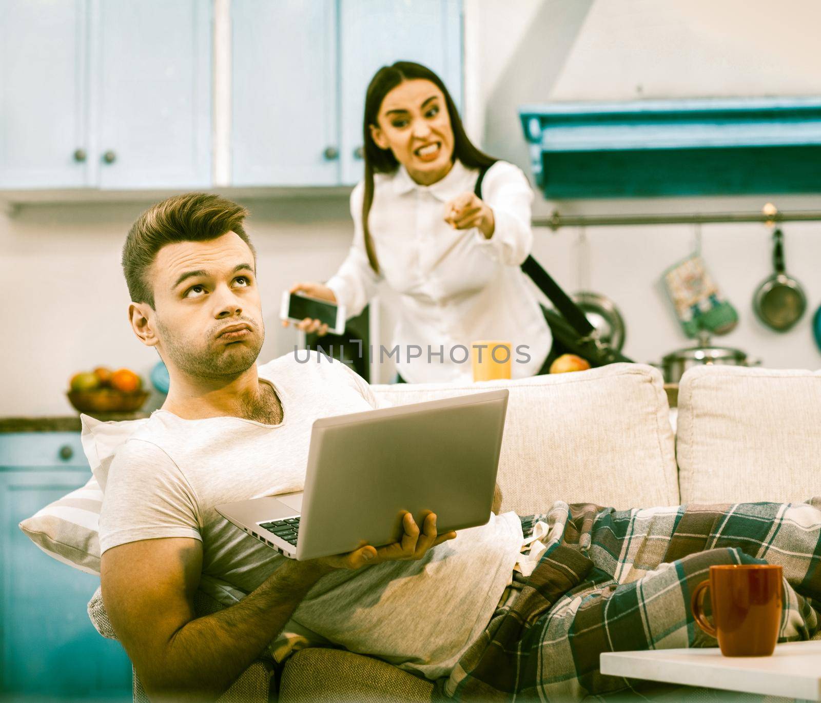 Family Conflict During Home Self-Isolation, Young Wife Is Angry That She Is Bored Of Sitting At Home, Her Husband Makes Displeased Face Lying On Sofa With Computer, Toned Image