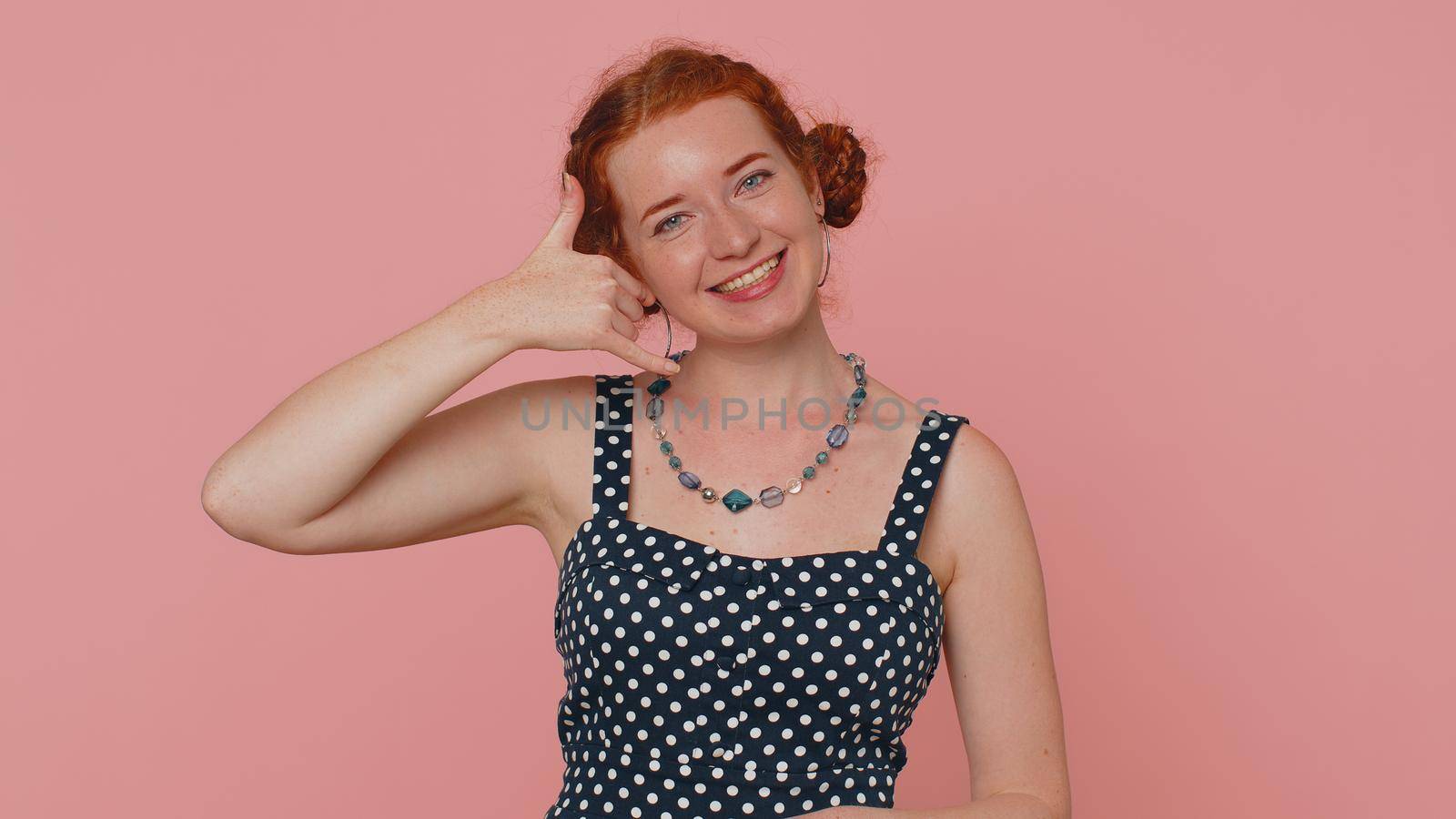 Call us, here is contact number. Redhead young woman seller looking at camera doing phone gesture like says hey you call me back. Adult ginger girl indoors studio shot isolated on pink background