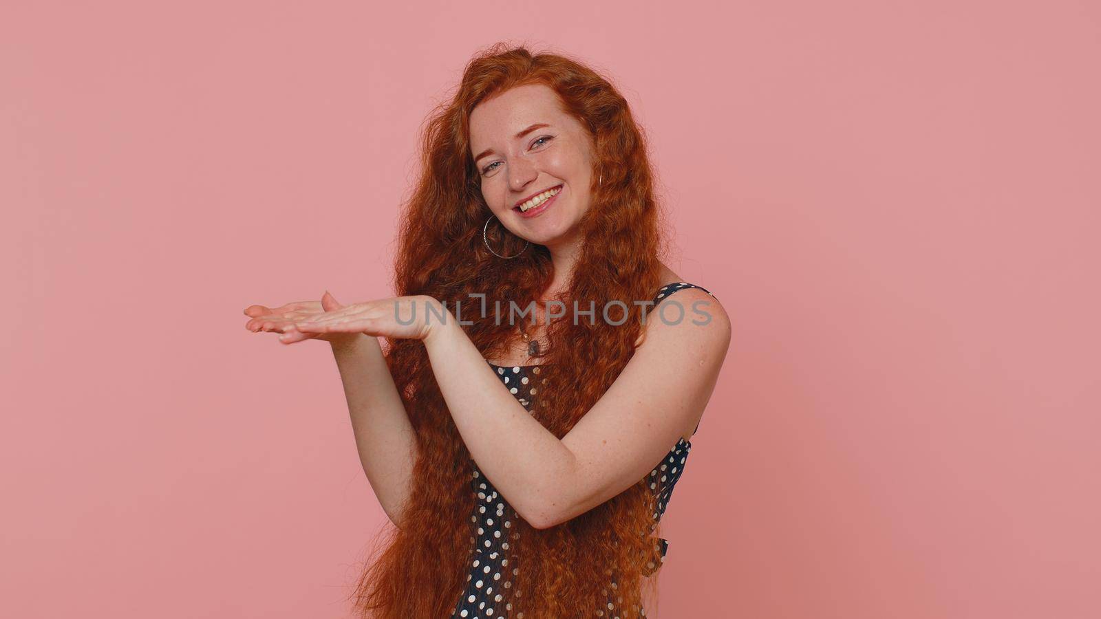 Cheerful rich redhead woman showing wasting or throwing money around hand gesture, more tips dreaming about big profit body language. Young freckles cute girl posing isolated on pink studio background