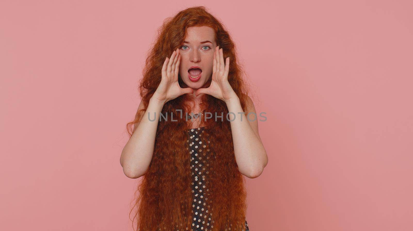 Expressive woman holding hands near mouth loudly screaming, shouting, yelling, announces discounts sale Hurry up, welcomes someone hello. Young redhead girl isolated alone on pink studio background