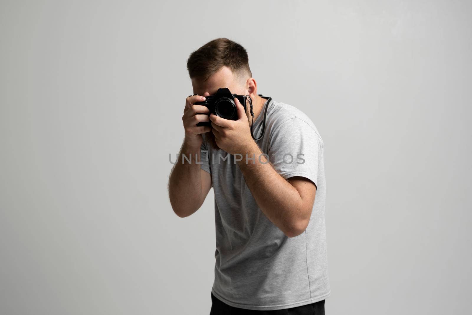 Handsome and confident man photographer with a large professional camera taking pictures photo shooting on the on the white background