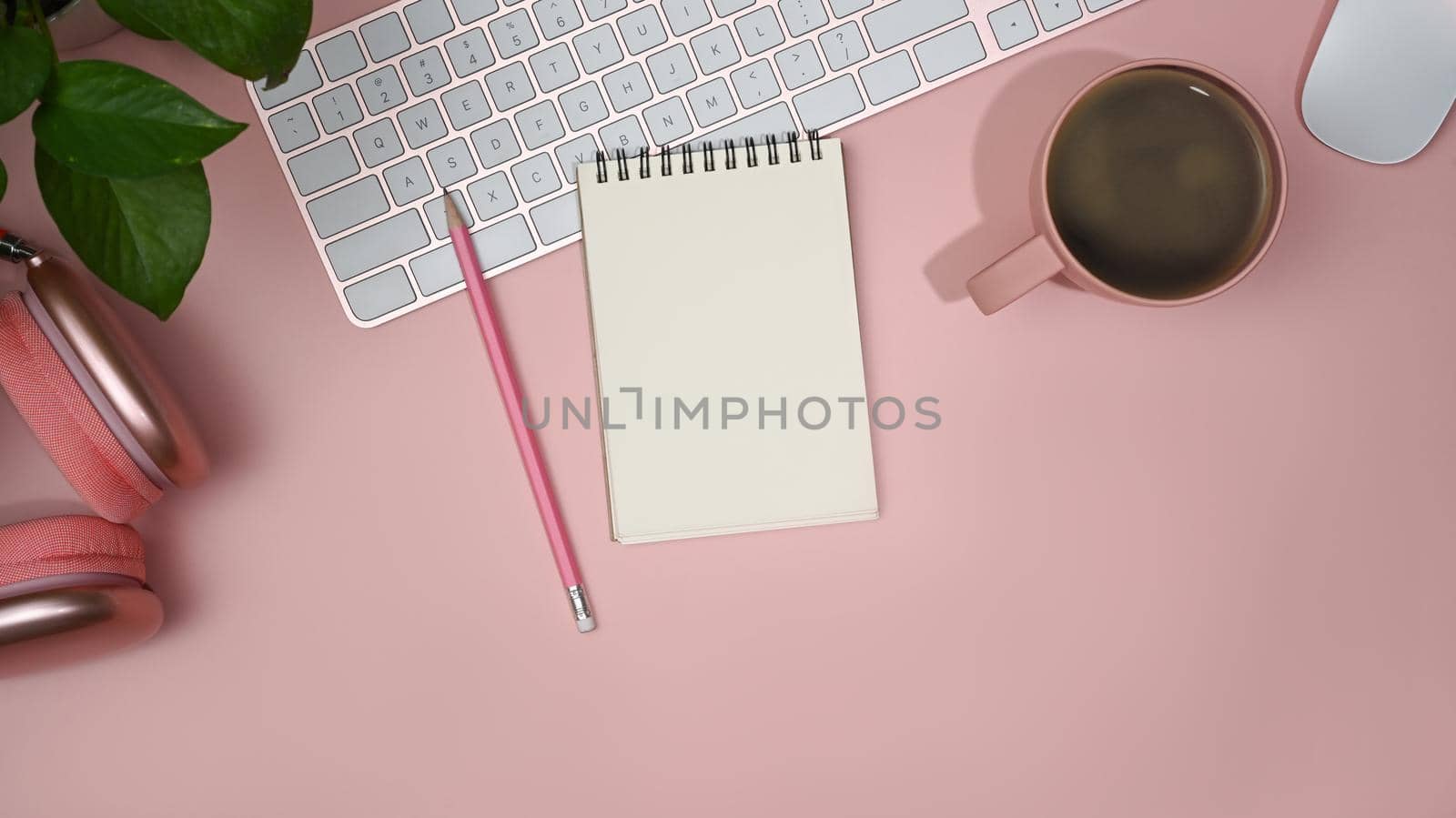 Flat lay blank notebook, wireless headphone and coffee cup on pink background. Feminine workplace.