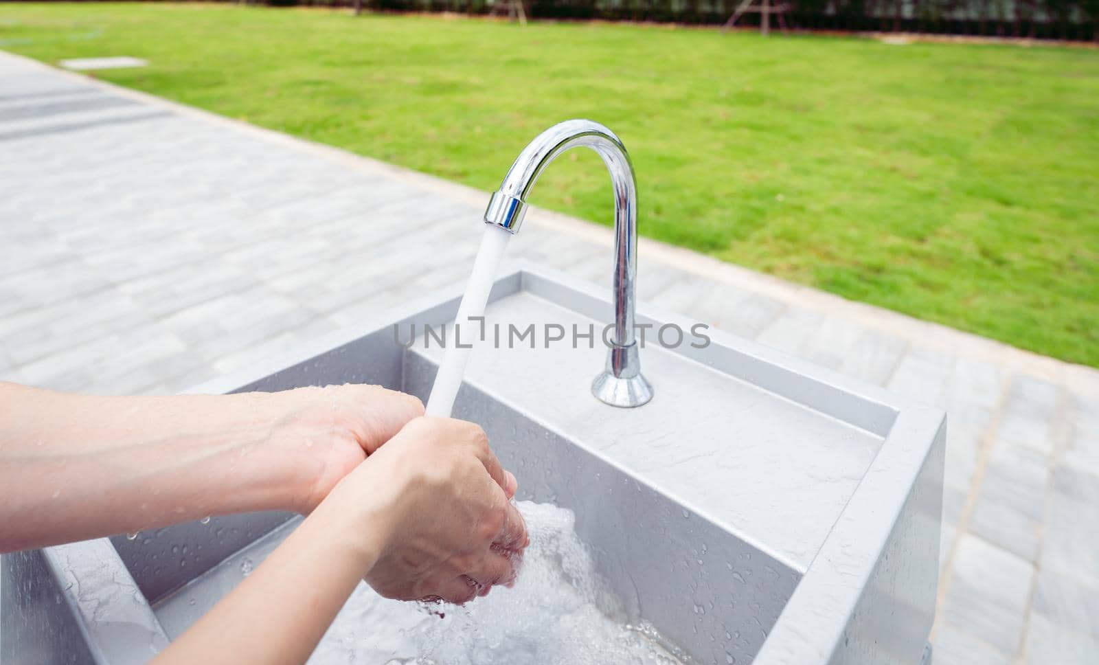 Woman washing hands with tap water under faucet at white sink. Washing hands with tap water at outdoor sink near grass field. Personal hygiene to prevent coronavirus or covid 19. Healthy lifestyle.
