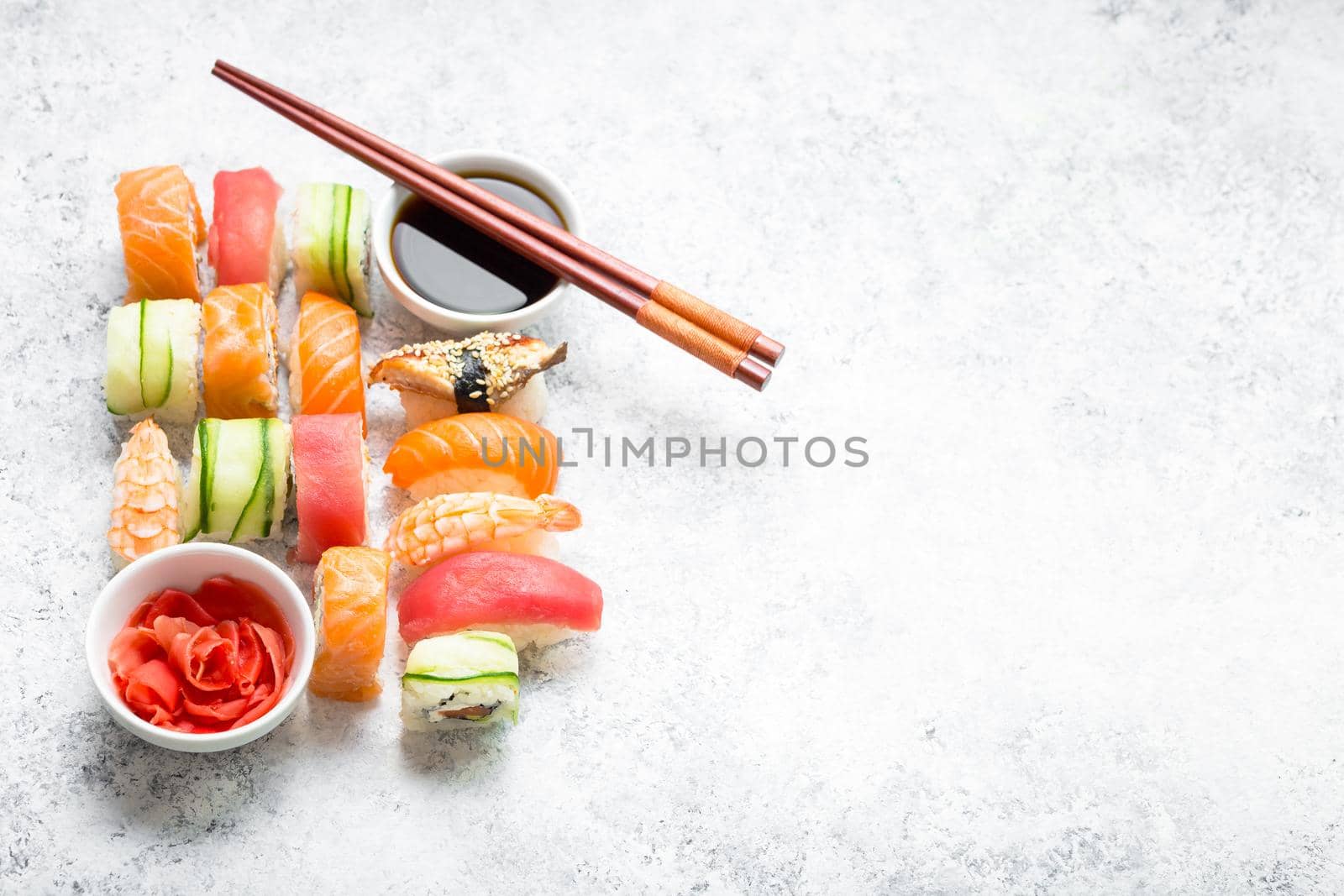 Assorted sushi set on white concrete background. Space for text. Japanese sushi, rolls, soy sauce, ginger, chopsticks. Top view. Sushi nigiri. Japanese dinner/lunch. Food frame. Different sushi mixed