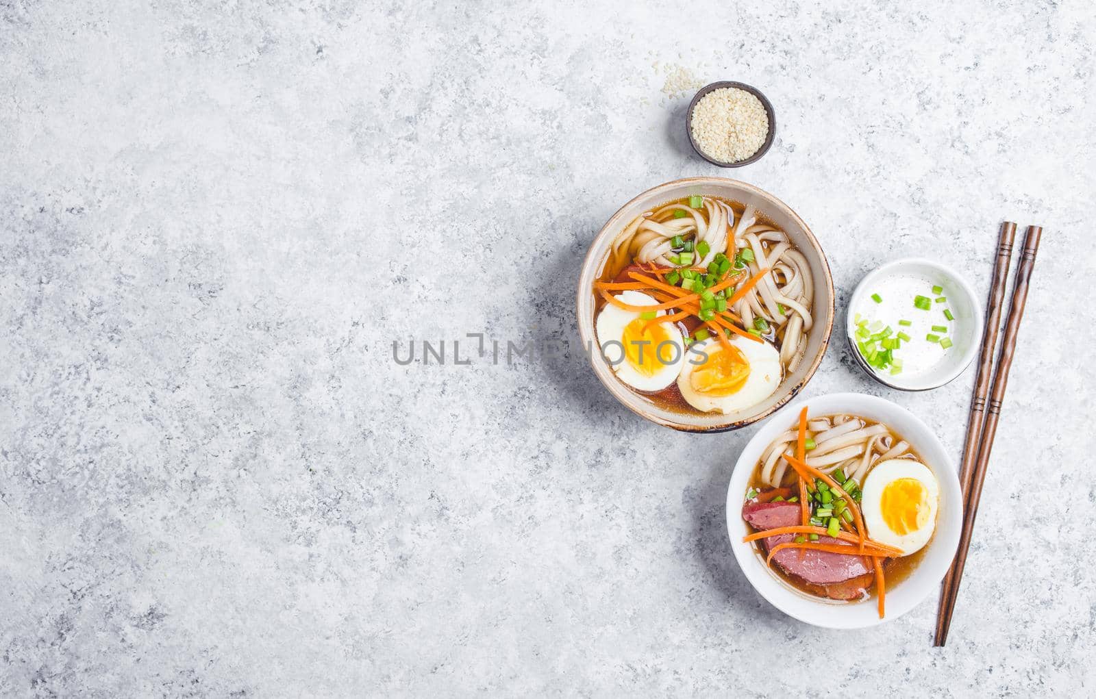 Bowls with Japanese soup ramen, chopsticks, white concrete rustic background. Traditional Asian soup with noodles, meat, eggs. Asian food. Japanese ramen for dinner. Space for text. Ramen, top view