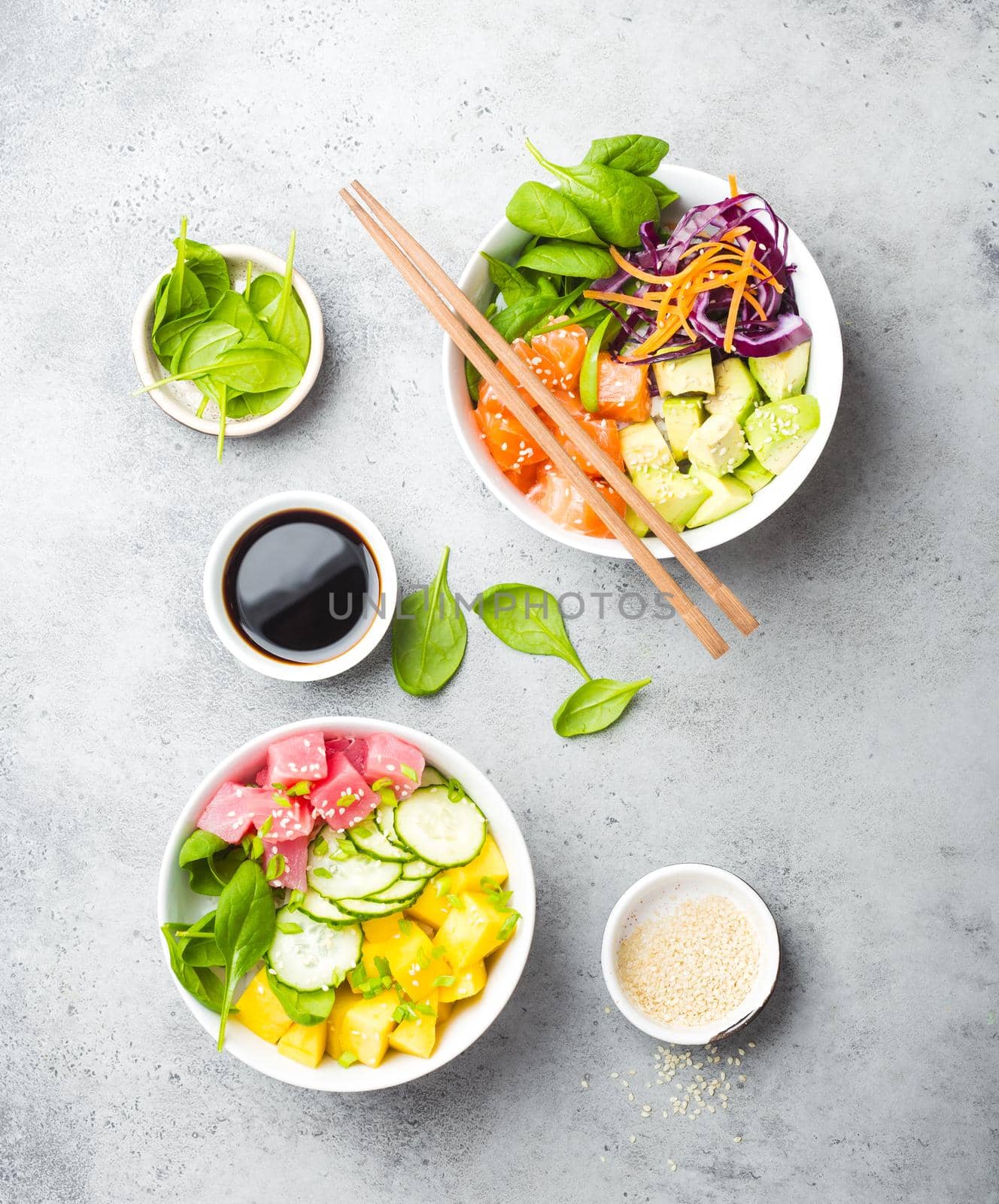 Two assorted poke bowls, raw tuna, salmon, vegetables, fruit. Top view. Traditional Hawaiian dish, rustic stone background. Healthy and clean eating concept. Poke with slices of raw fish, chopsticks